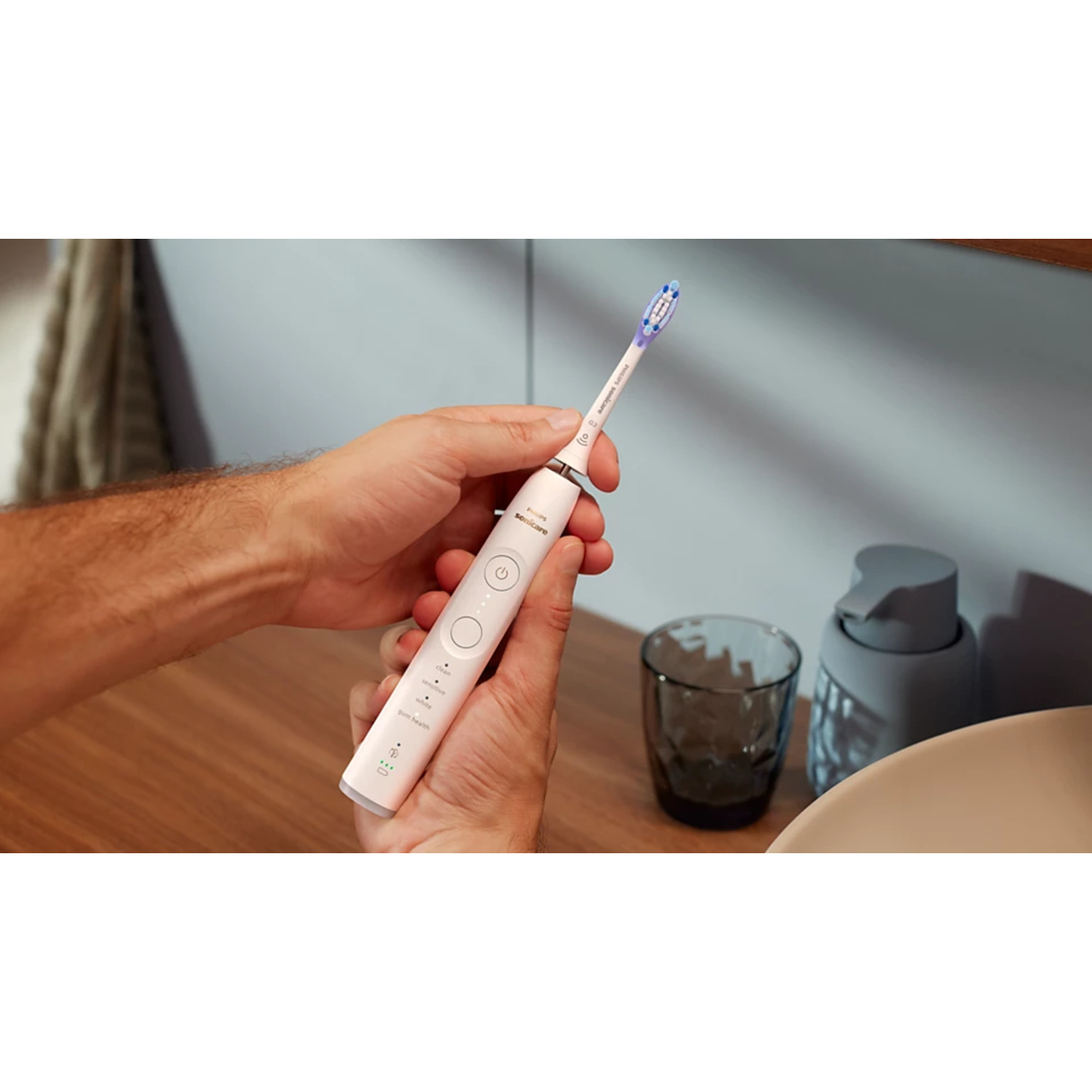 Personne tenant une brosse à dents électrique, cadre de salle de bain, fond blanc.