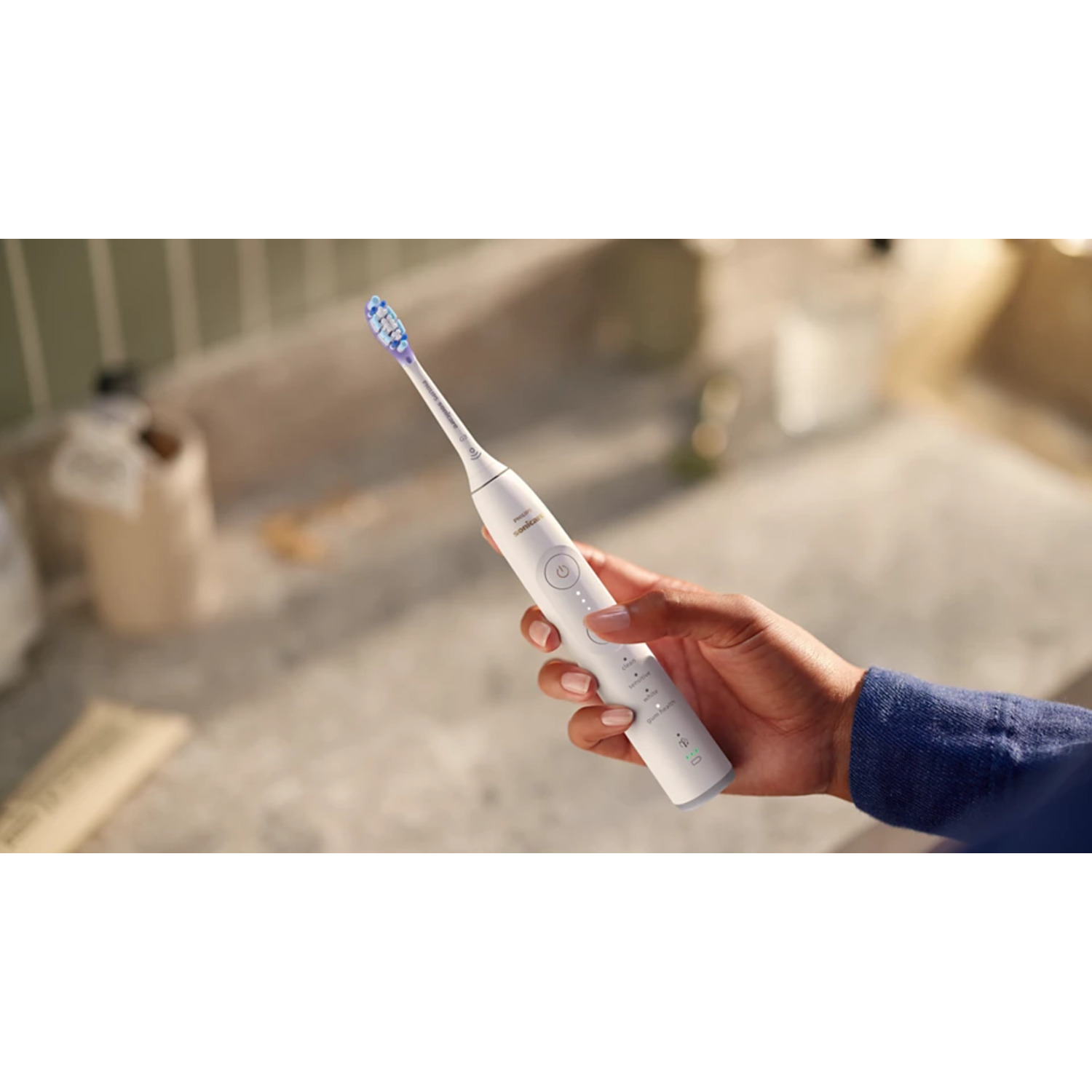 Une main tenant une brosse à dents électrique blanche avec une tête de brosse bleue et blanche.