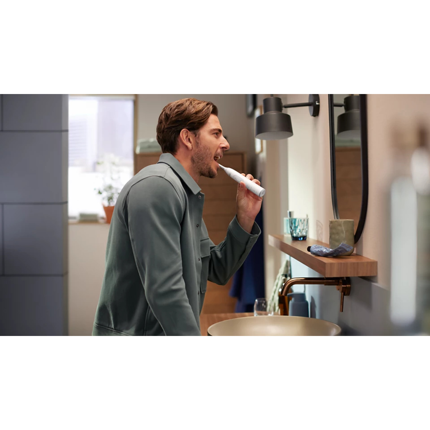 Homme se brossant les dents dans une salle de bain avec miroir, lavabo et articles de toilette sur une étagère.