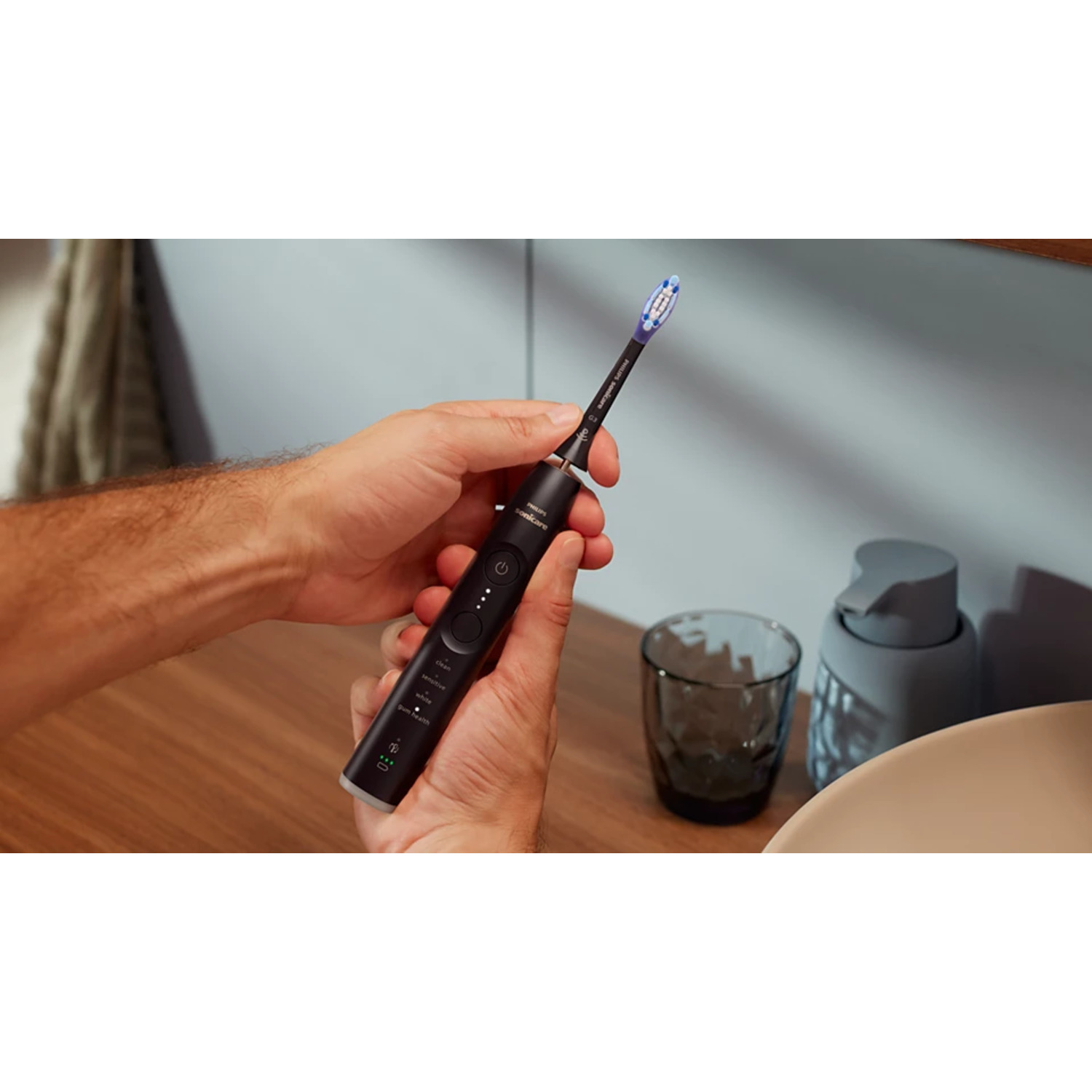 Mains tenant une brosse à dents électrique noire au-dessus d'un évier. La brosse a une tête de brosse bleue.