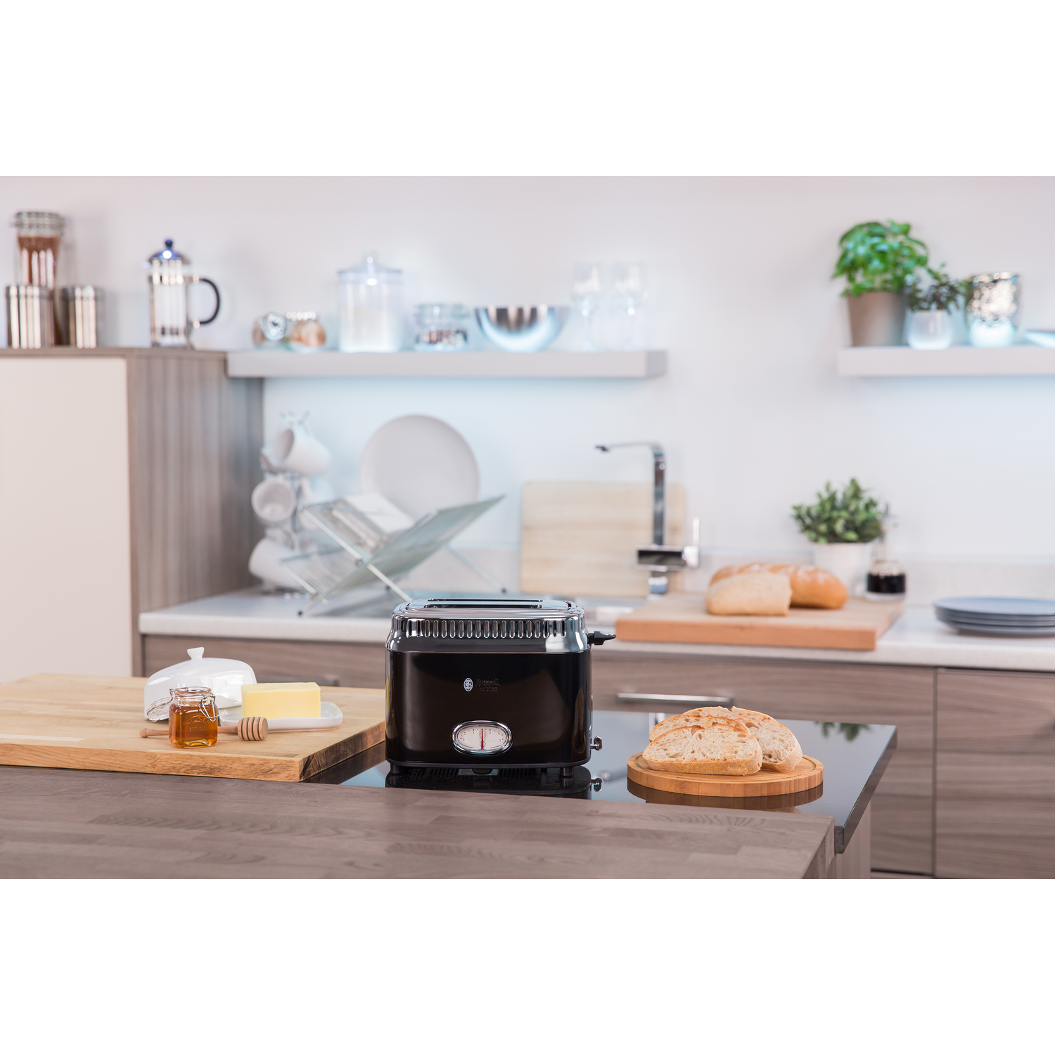 A black toaster on a countertop with bread, honey, and butter. A wooden cutting board is next to it.