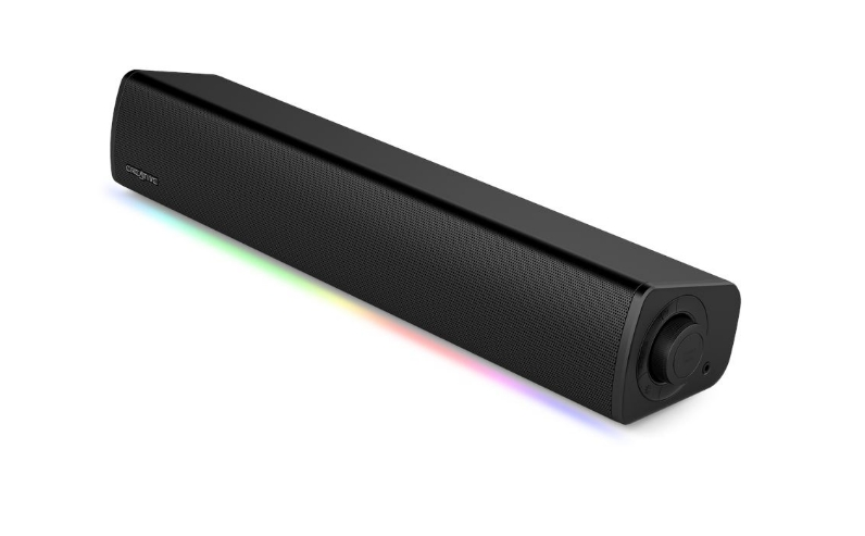 Czarny głośnik soundbar z siatkowym przodem. Posiada pokrętło głośności i kolorowy pasek świetlny na dole.