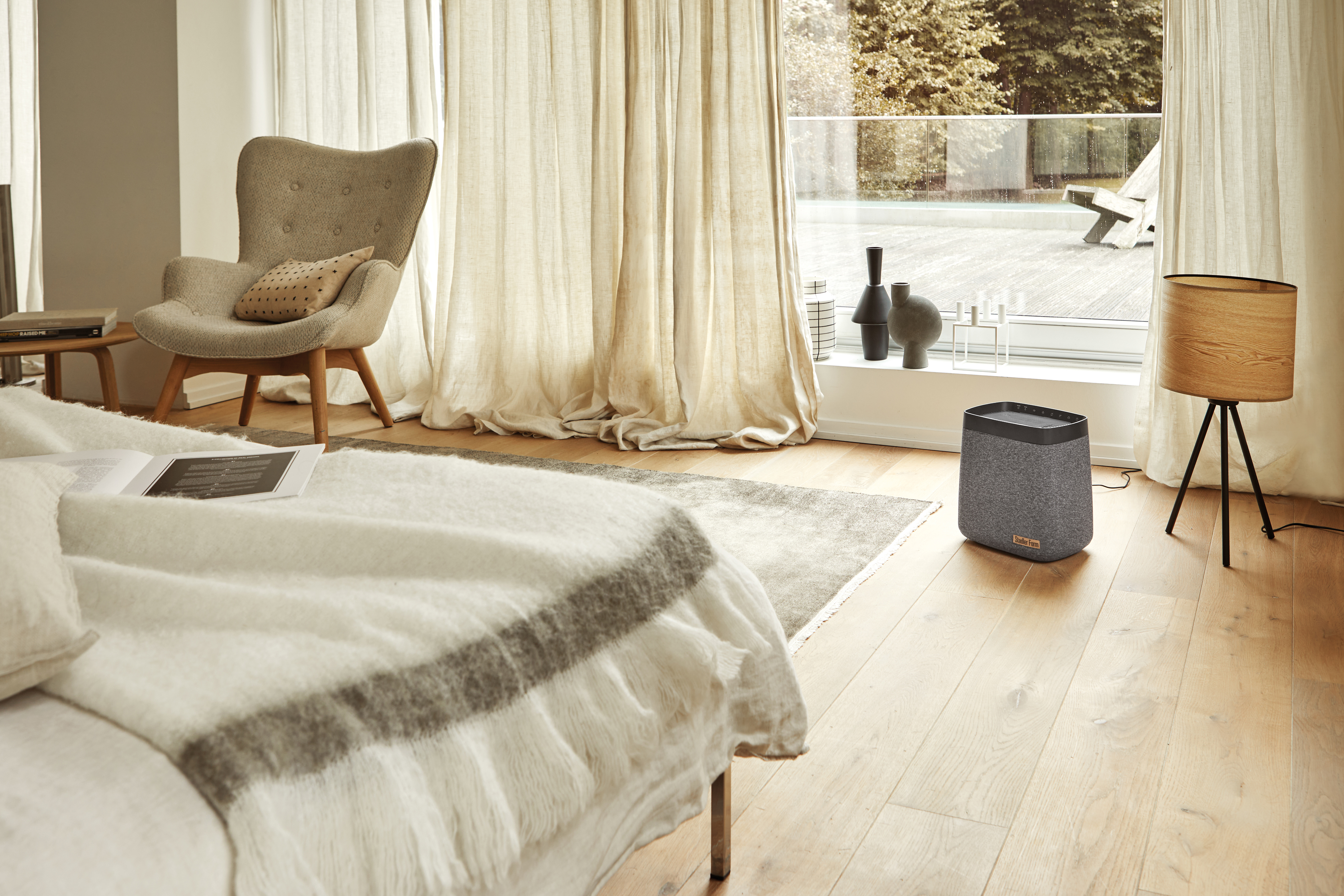 Schlafzimmer mit Bett, Lampe und grauem Luftreiniger.