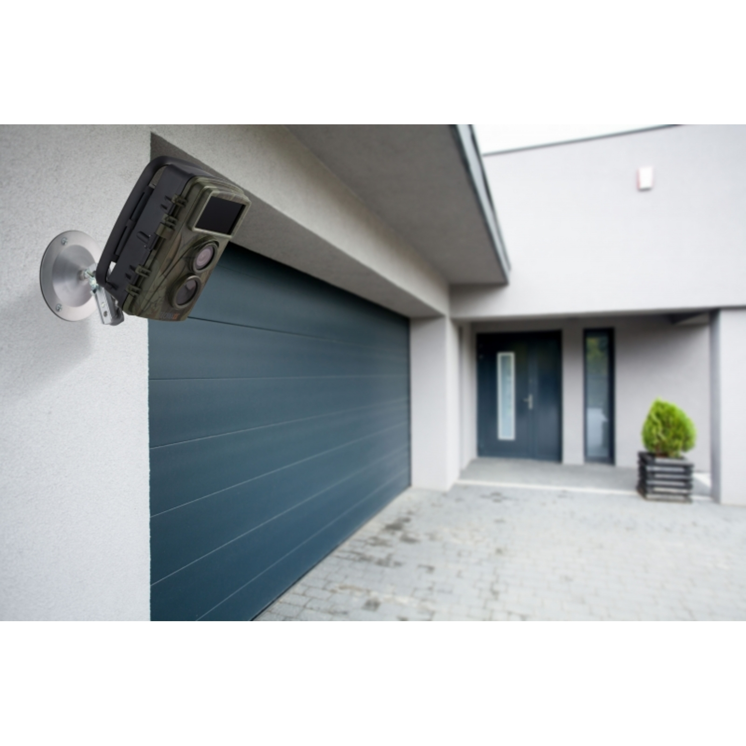 Caméra de sécurité fixée au mur. Maison grise et porte de garage verte en arrière-plan.
