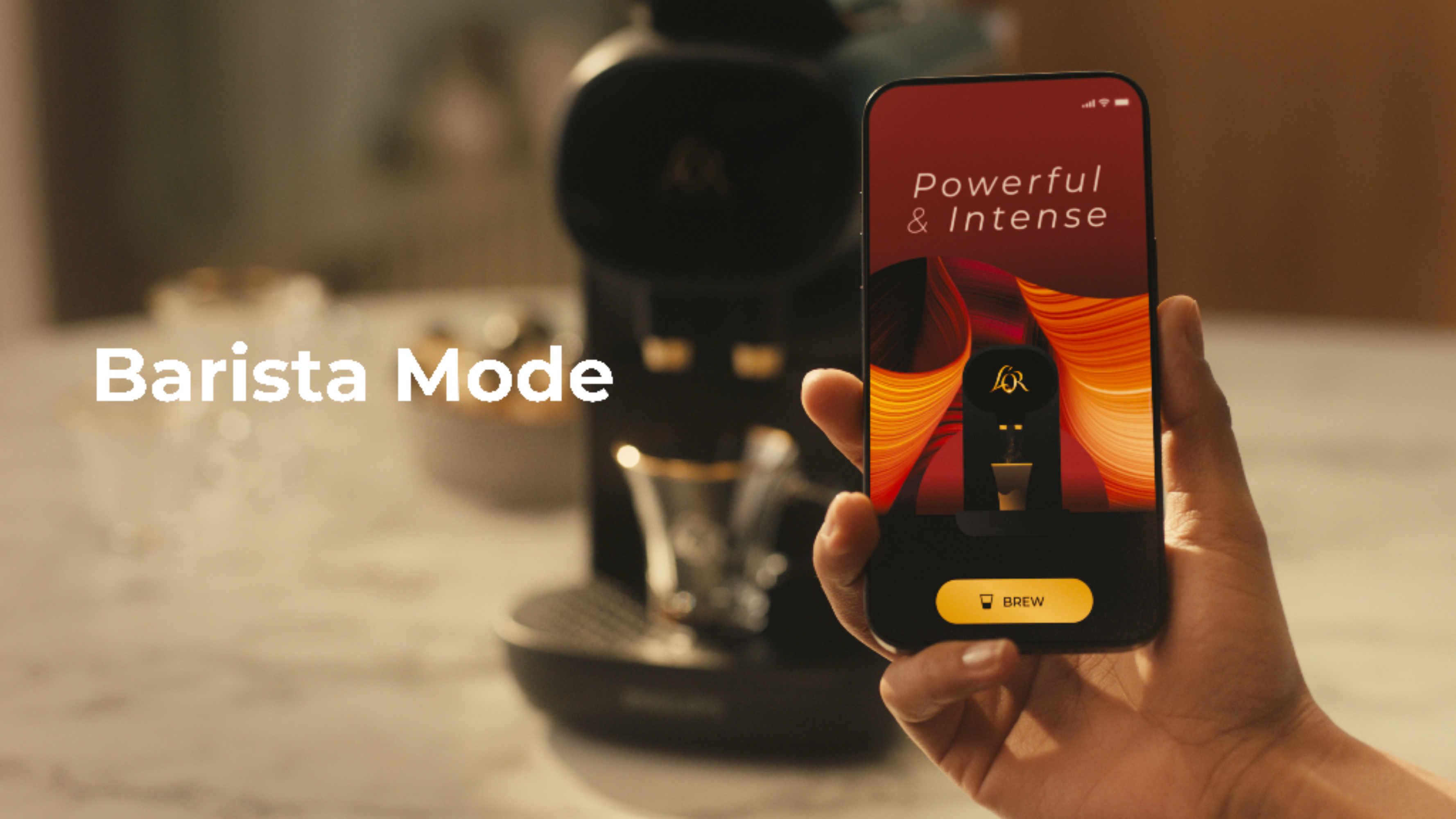 Una persona sostiene un teléfono que muestra el 'Modo Barista' en una cafetera. El teléfono tiene un botón 'Brew'.