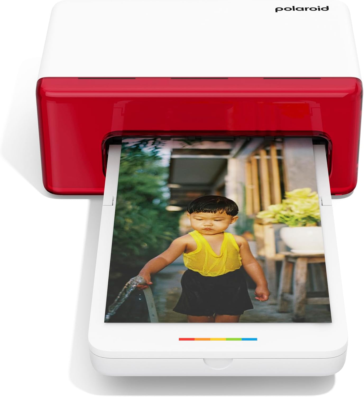 Impresora de fotos Polaroid imprimiendo una foto. Un niño de amarillo sostiene una manguera, al aire libre.