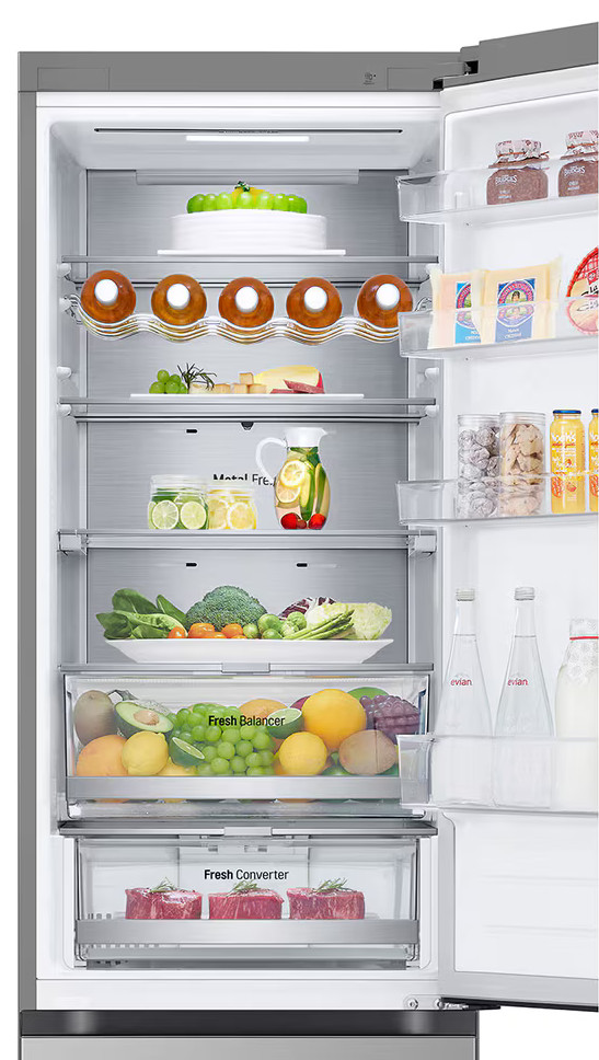 Otwarta lodówka wypełniona produktami spożywczymi, w tym owocami, napojami i serem.