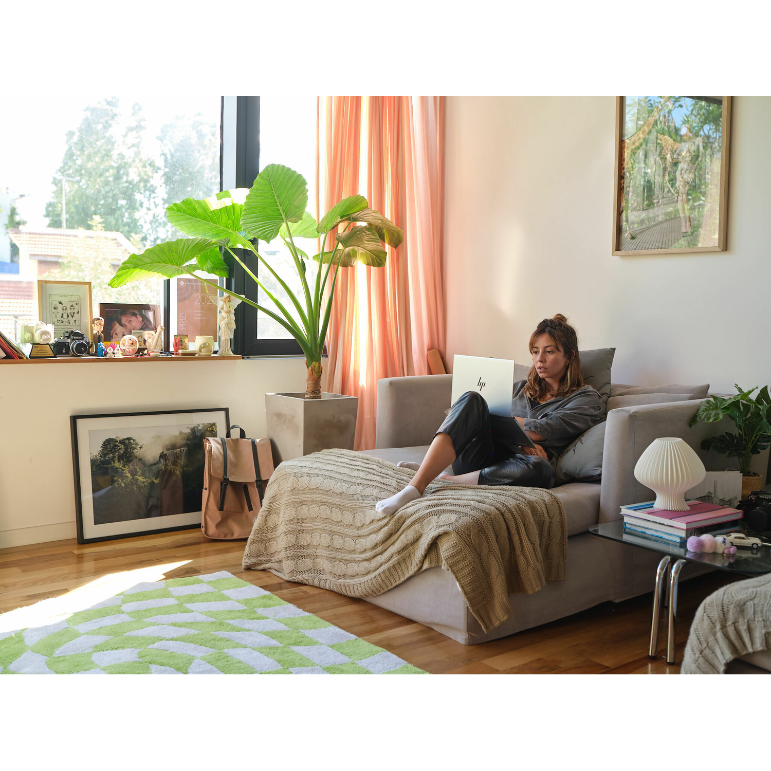 Vrouw die een laptop gebruikt op een bank. Een plant en een fotolijst staan op de achtergrond.