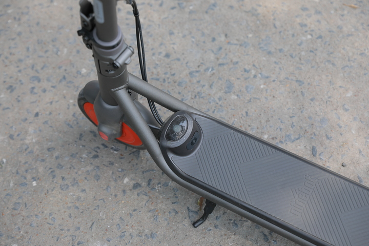 Szara i pomarańczowa hulajnoga Ninebot, zbliżenie na przód, na betonowej nawierzchni.