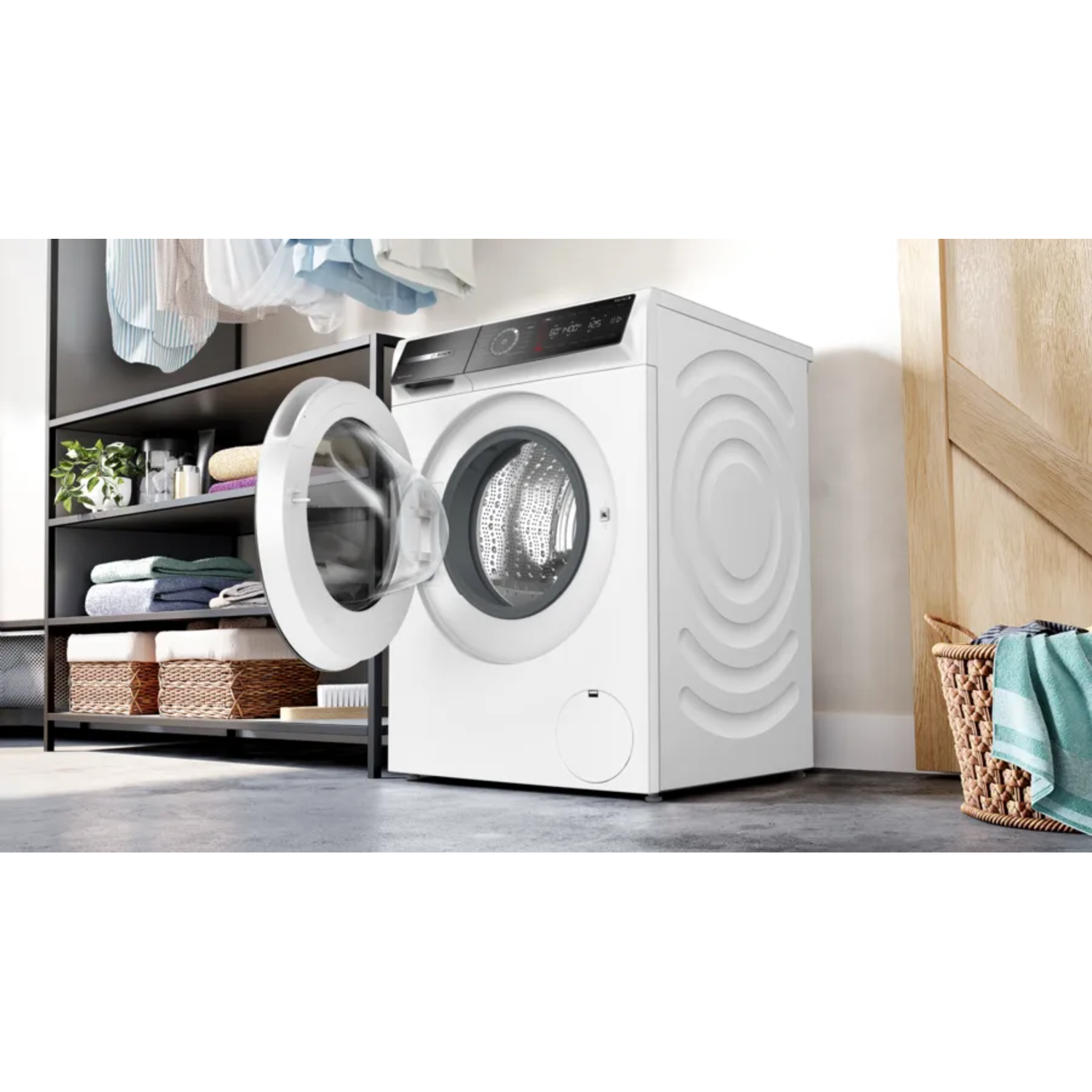 A white washing machine with an open door. Clothes are inside the drum. Shelves and a basket are in the background.