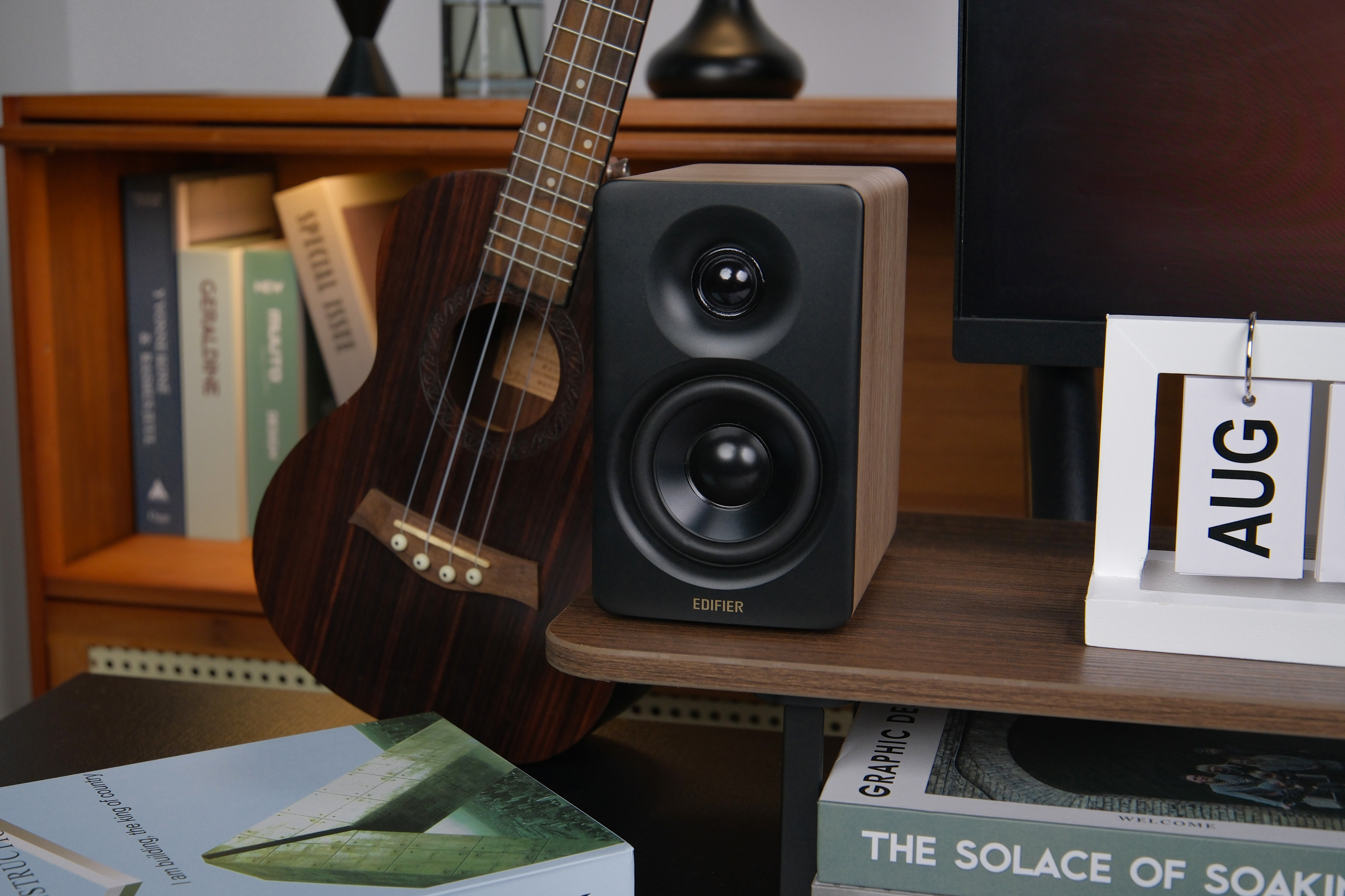 Ein Lautsprecher auf einem Regal mit Gitarre und Büchern im Hintergrund und einem Kalender.
