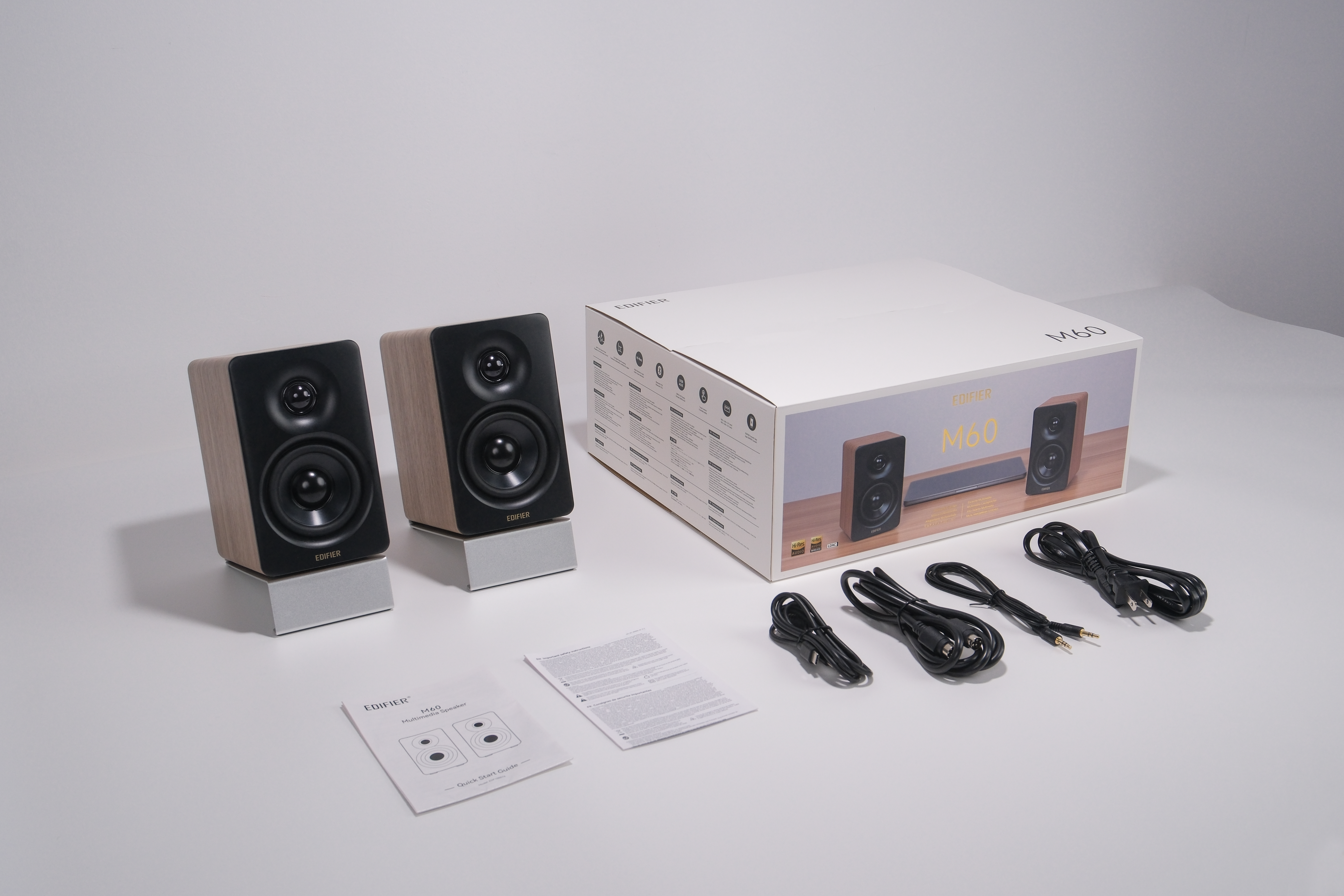Zwei hölzerne Lautsprecher, eine weiße Box, Kabel und Anweisungen auf weißer Oberfläche.