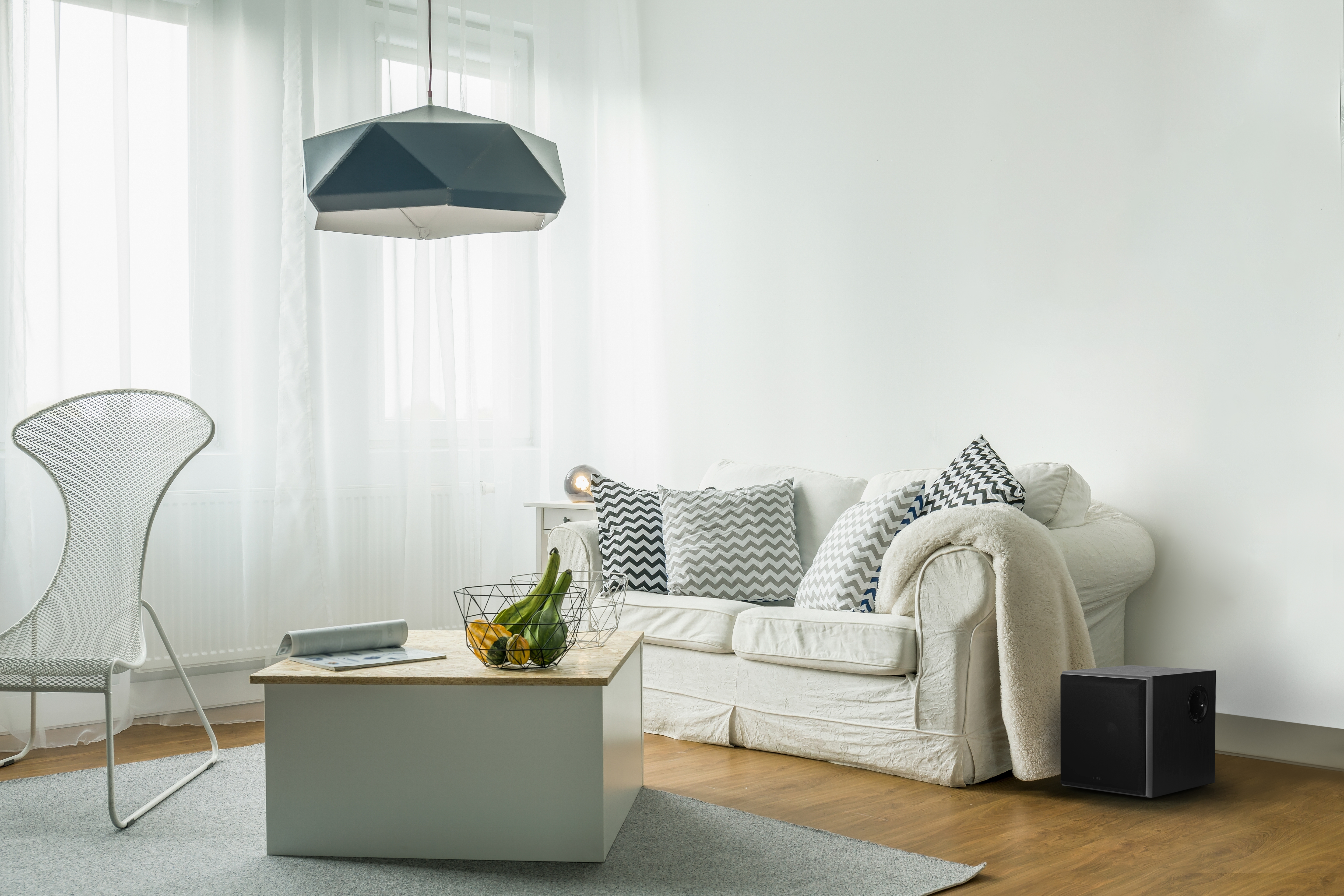 Ein weißes Sofa mit Kissen, ein Couchtisch mit Dekoration und ein schwarzer Subwoofer in einem weißen Raum.