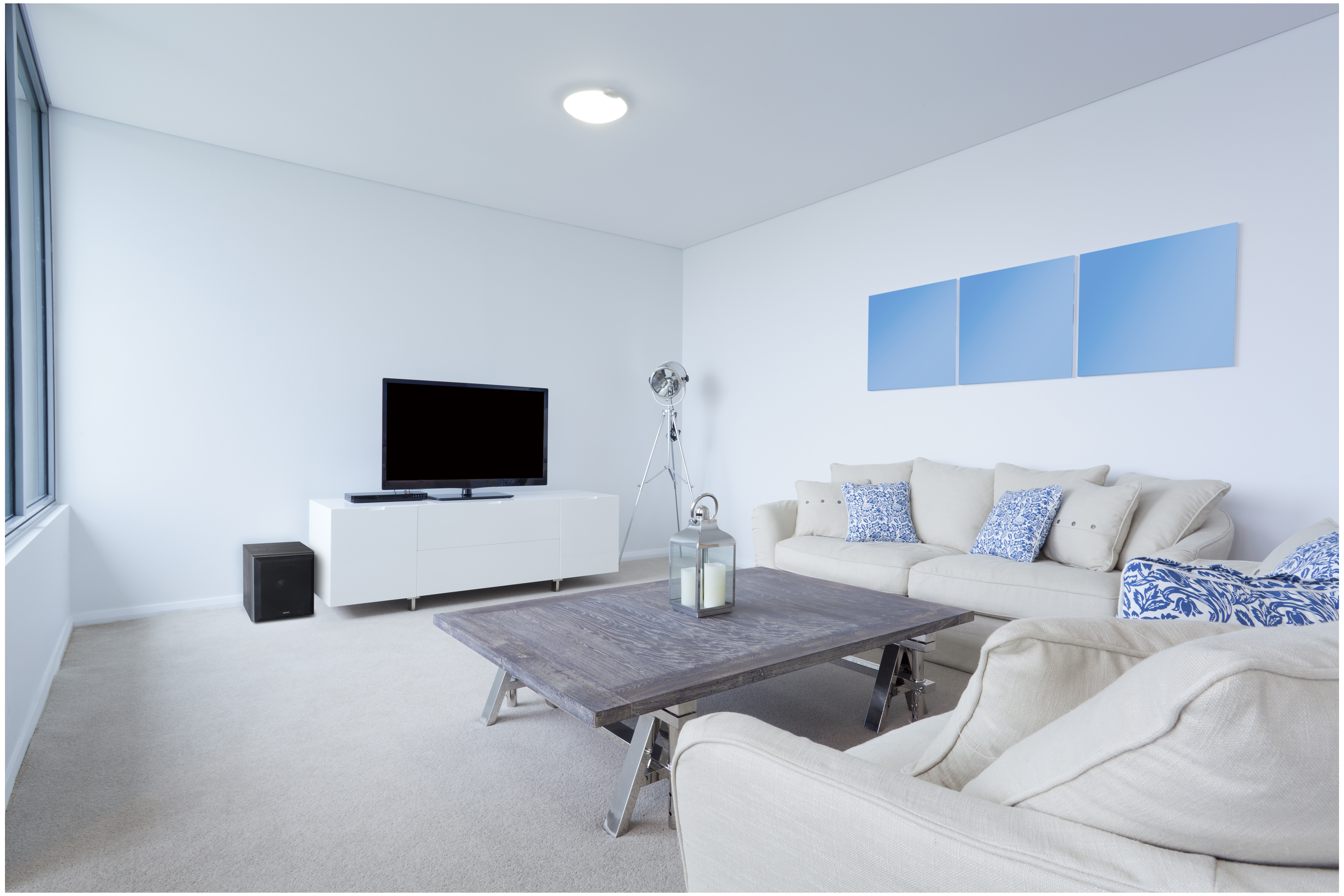 Wohnzimmer mit TV, Sofa, Beistelltisch und drei blauen Kunstwerken.