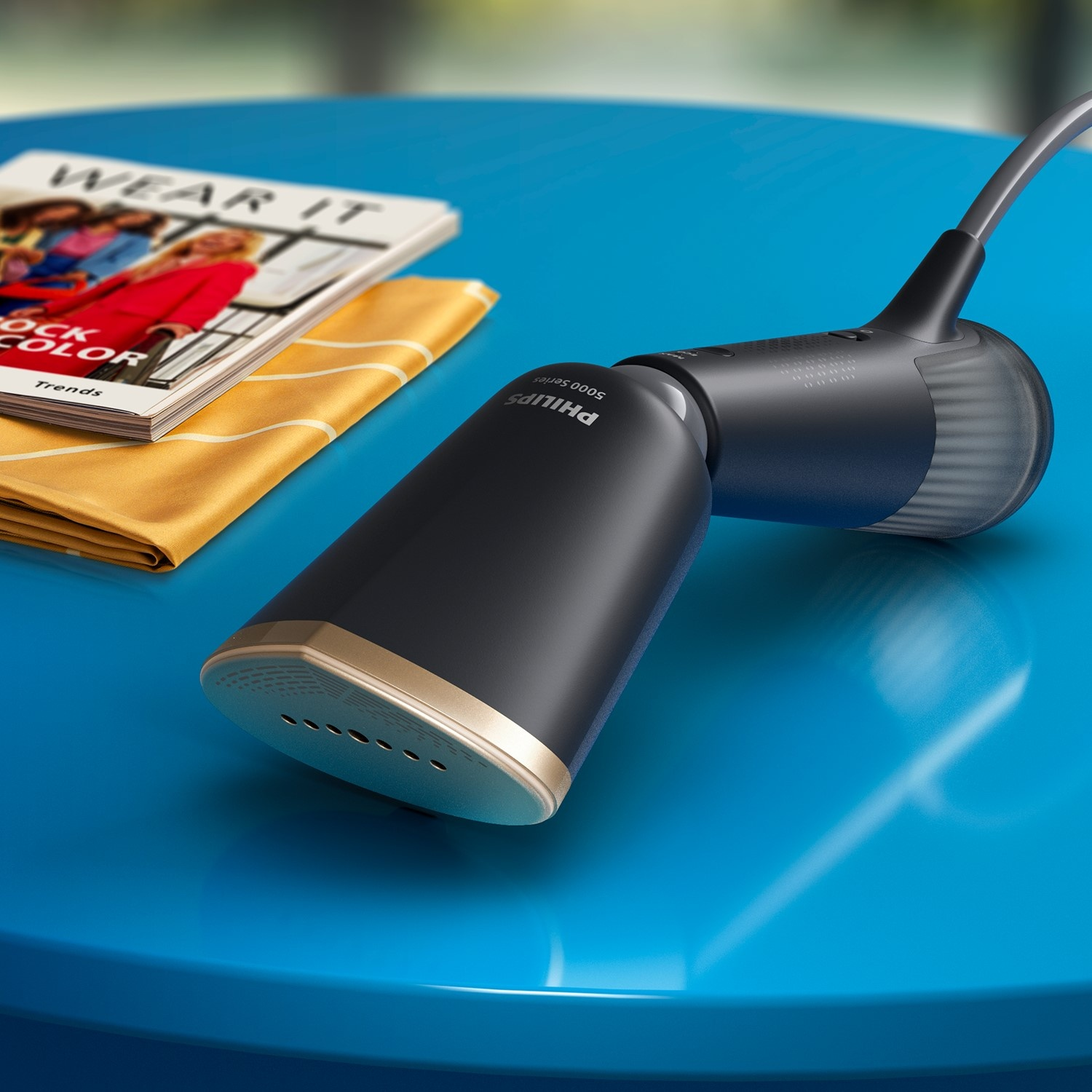 Vaporiera Philips nera e oro su tavolo blu con rivista.