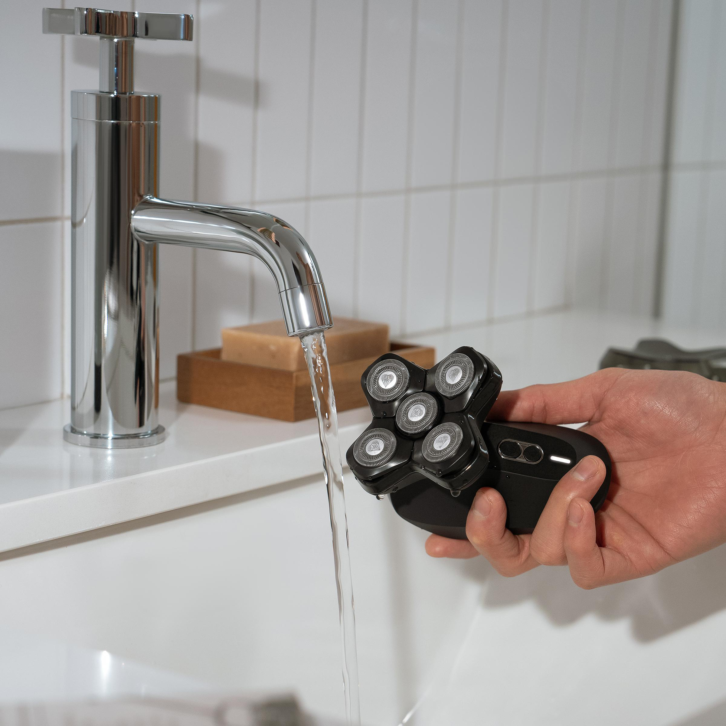 Eine Person hält einen schwarzen Elektrorasierer unter fließendem Wasser in einem Badezimmer.