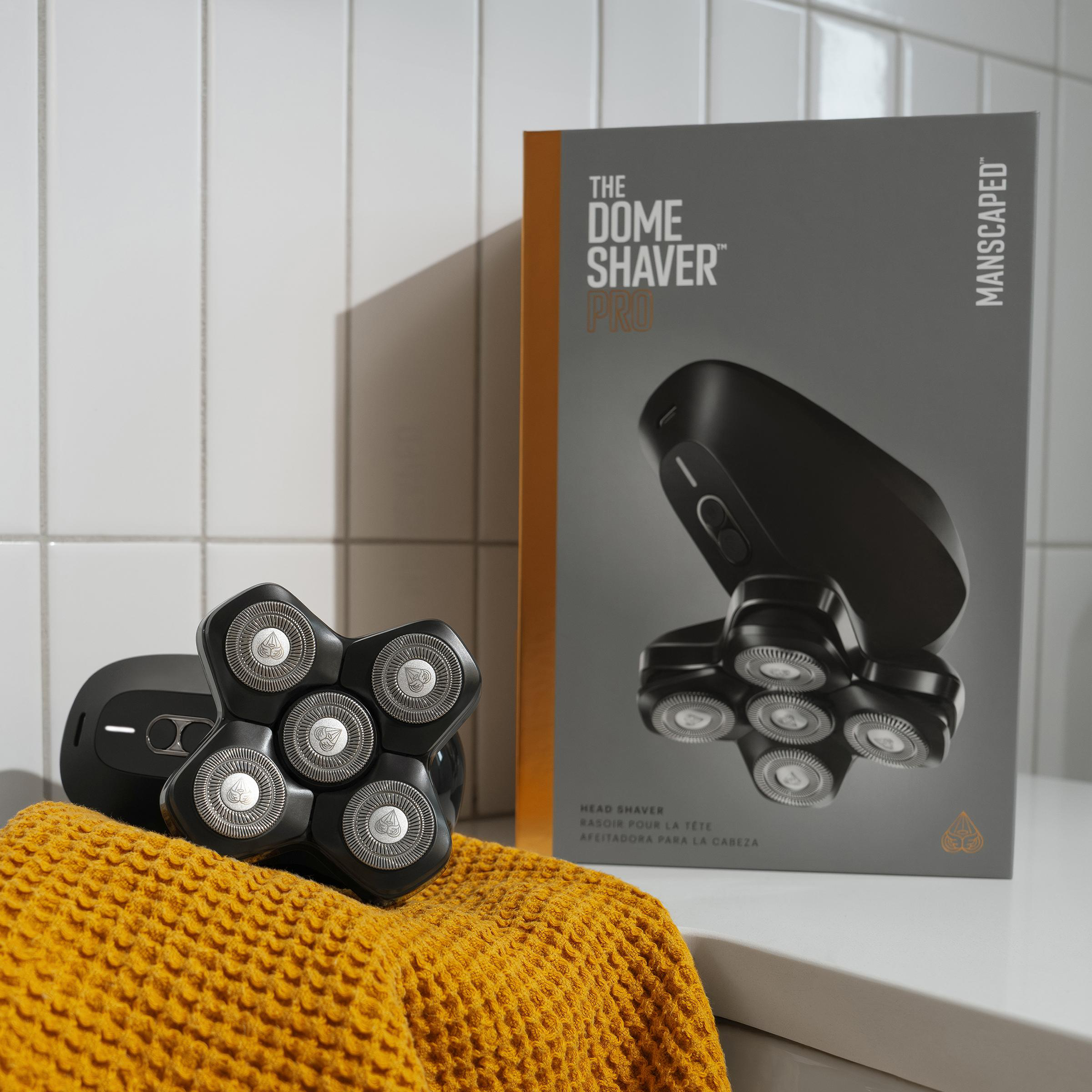 Ein schwarzer Elektrorasierer und eine Schachtel liegen auf einer weißen Oberfläche. Ein gelbes Handtuch ist in der Nähe.