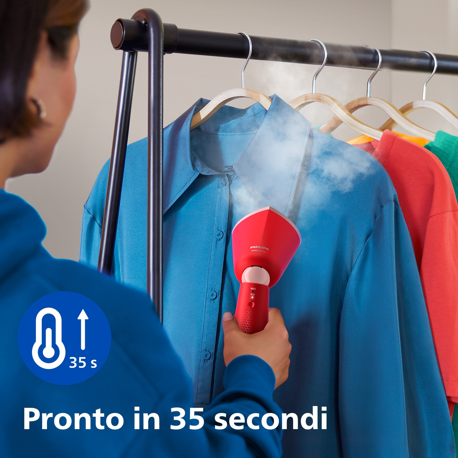 Una persona che stira una camicia blu con un vaporizzatore rosso su un attaccapanni.