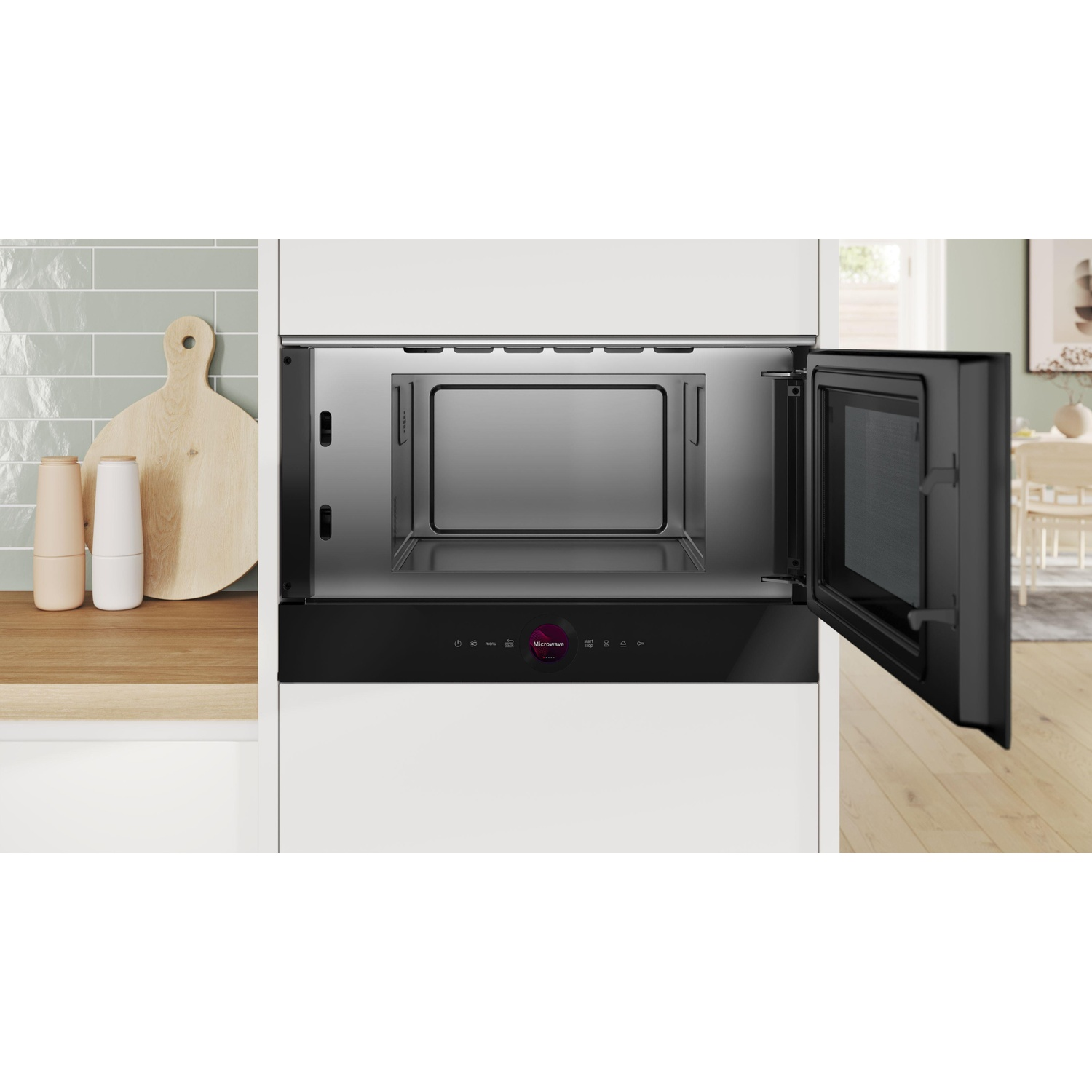 Un forno a microonde nero è aperto. All'interno c'è un interno in metallo. A sinistra c'è un tagliere.