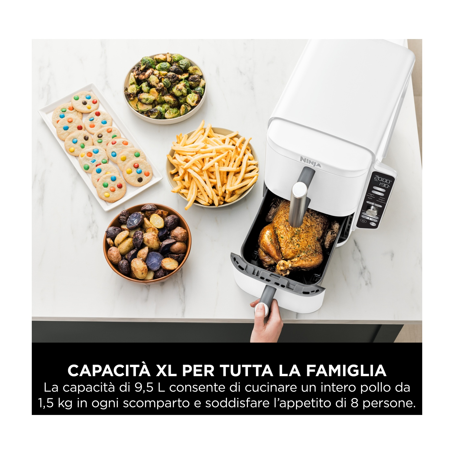 Una friggitrice ad aria con un pollo cotto e contorni. Il cibo è su una superficie bianca.