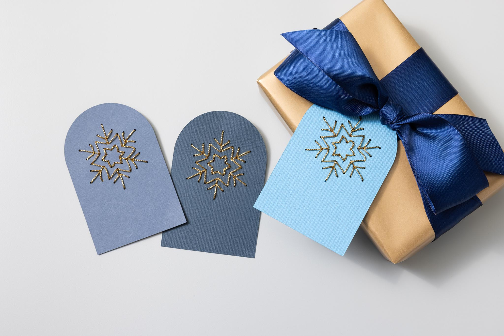 Drei blaue und graue Karten mit goldenen Schneeflocken, an eine Geschenkbox gebunden.