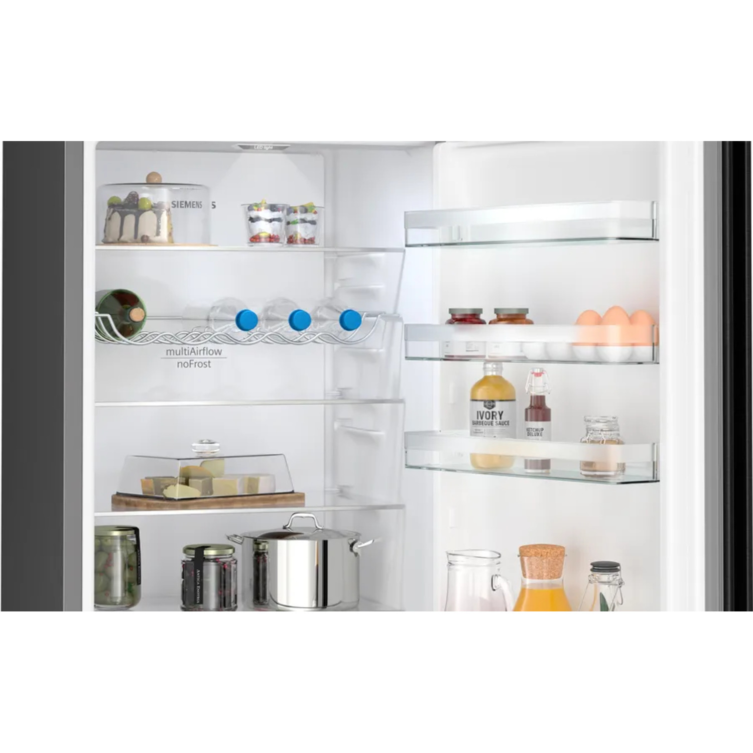 Open refrigerator with food items. Glass shelves, jars, and bottles. Cakes and eggs.