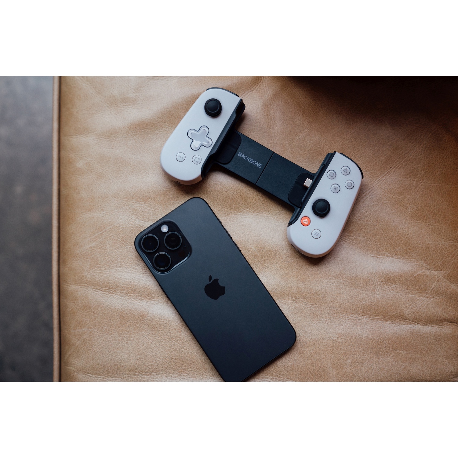 Black iPhone with a controller on a brown leather surface. The controller is black and white.
