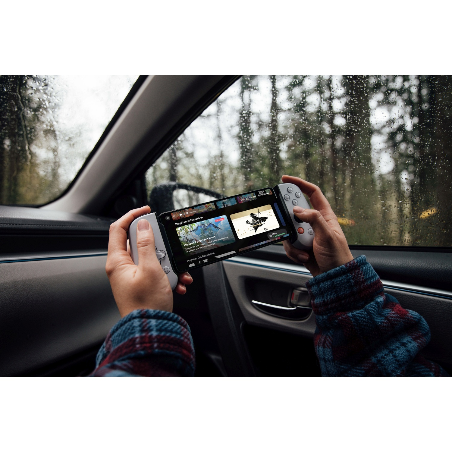 Hands holding a controller with a phone displaying a game inside a car.