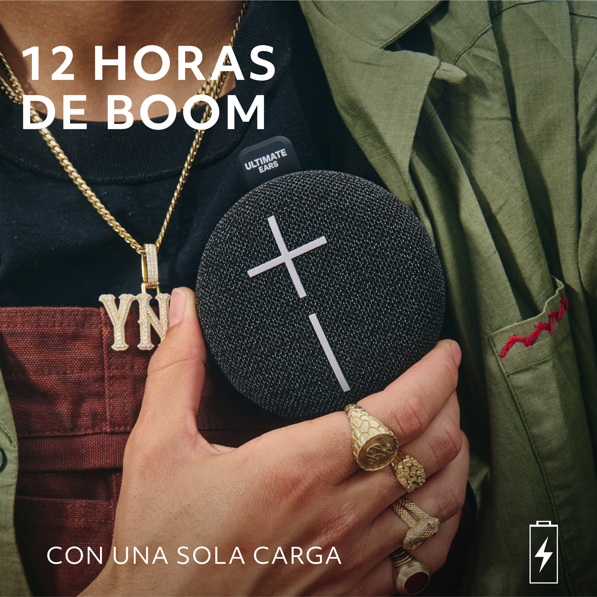 Una persona sosteniendo un altavoz negro con una cruz blanca, con joyas de oro.