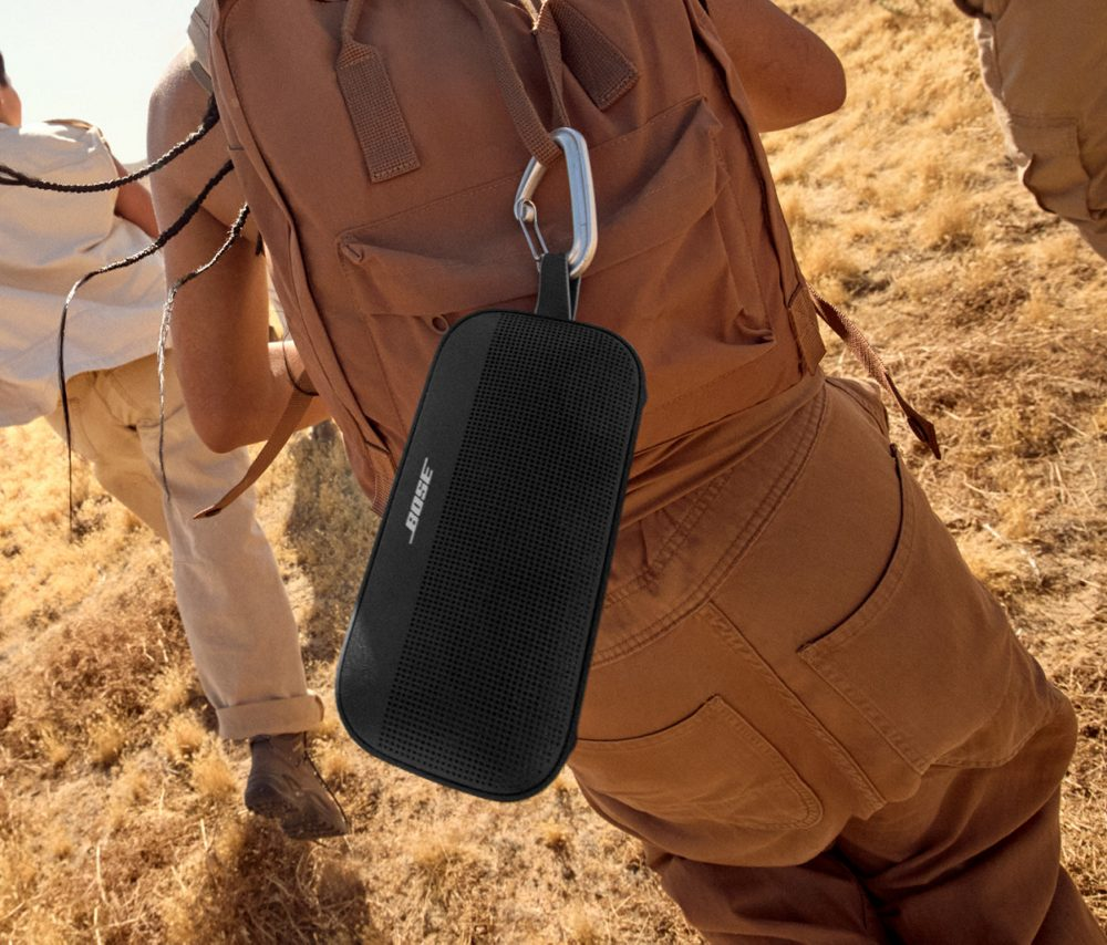 Osoba niesie czarny głośnik z karabińczykiem na plecaku.