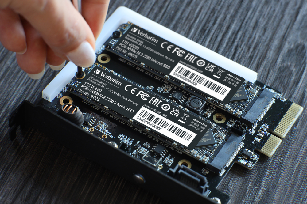 Bir el, siyah bir devre kartına monte edilmiş iki SSD sürücüsüne vidalar yerleştiriyor.