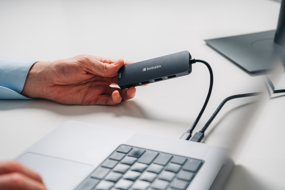 Bir kişinin eli, bir dizüstü bilgisayara bağlı bir Verbatim USB hub'ı tutuyor.