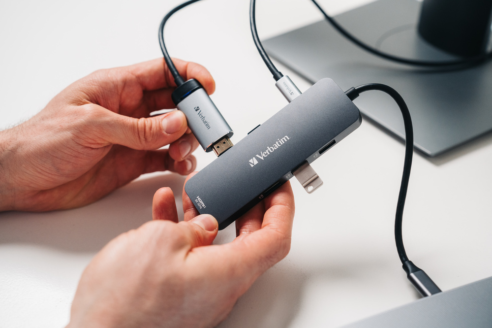 Eller, bir monitöre bağlı, HDMI ve diğer bağlantı noktalarına sahip bir Verbatim USB hub'ı tutuyor.