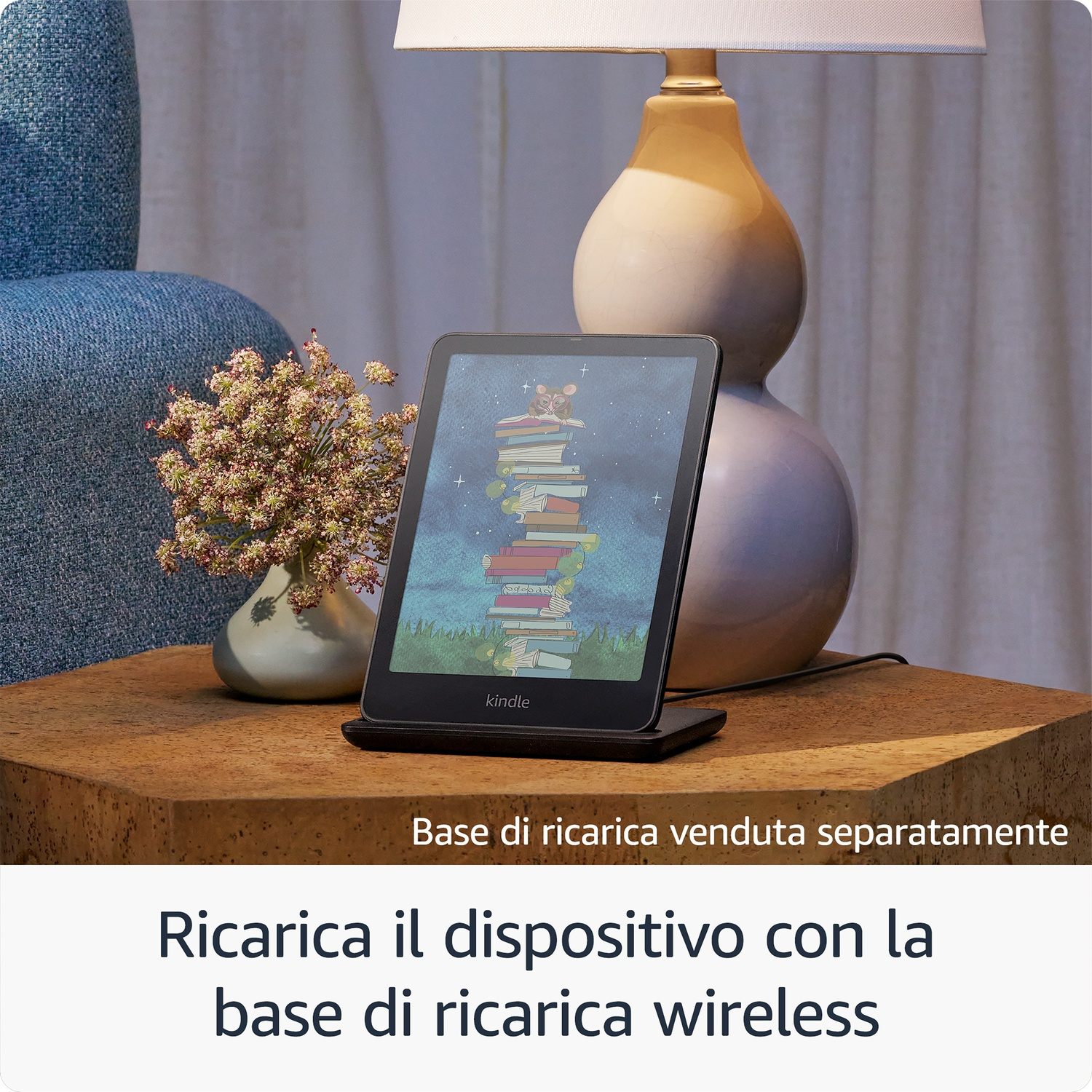 Dispositivo Kindle su una base di ricarica su un tavolo, con una lampada sullo sfondo. Testo in italiano.