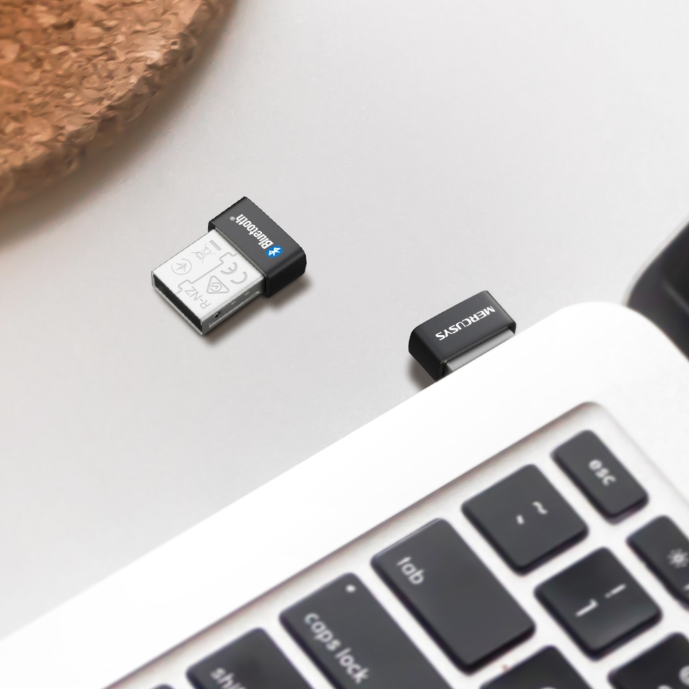 Beyaz bir masada bir Mercusys Bluetooth USB adaptörü ve bir dizüstü bilgisayar klavyesi.