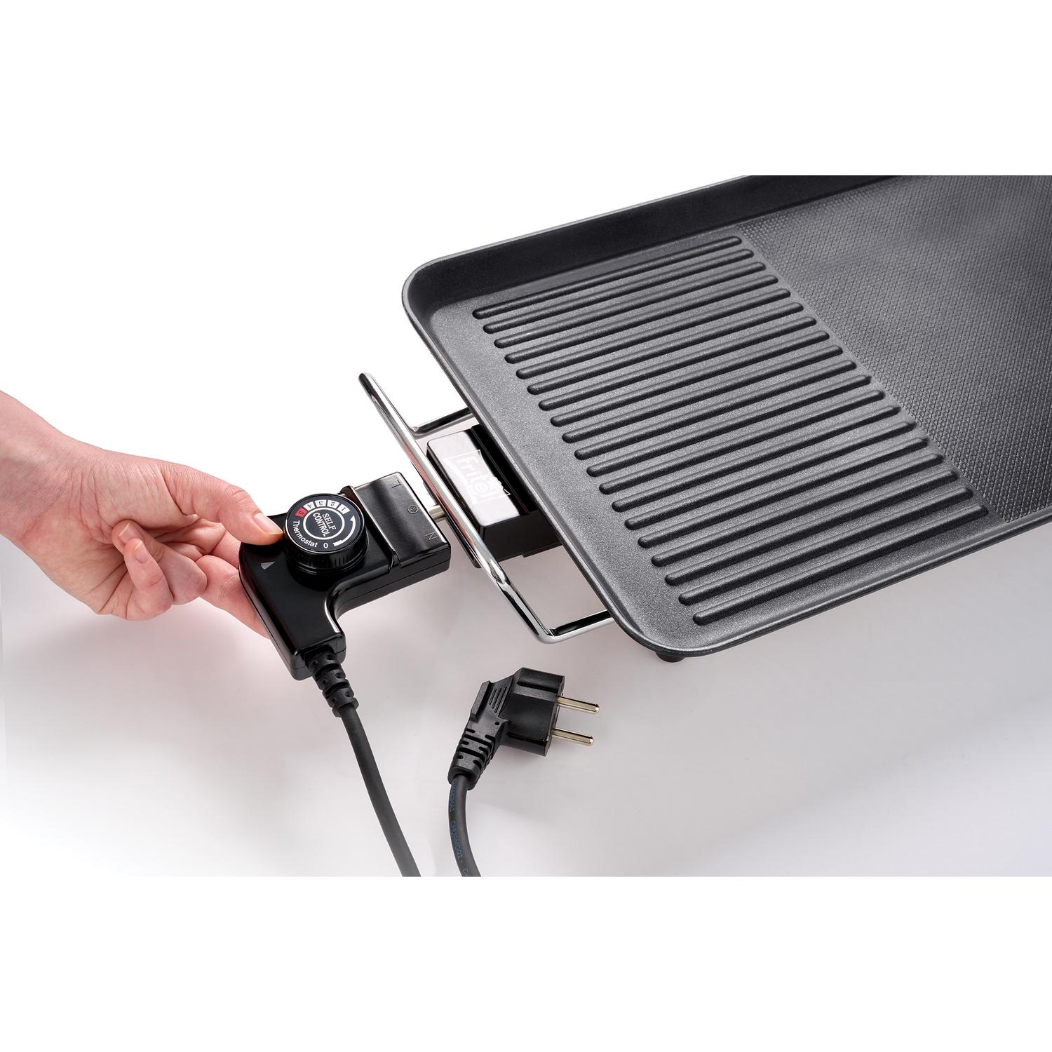 A hand adjusting the temperature control on an electric grill with a black handle and a power plug.