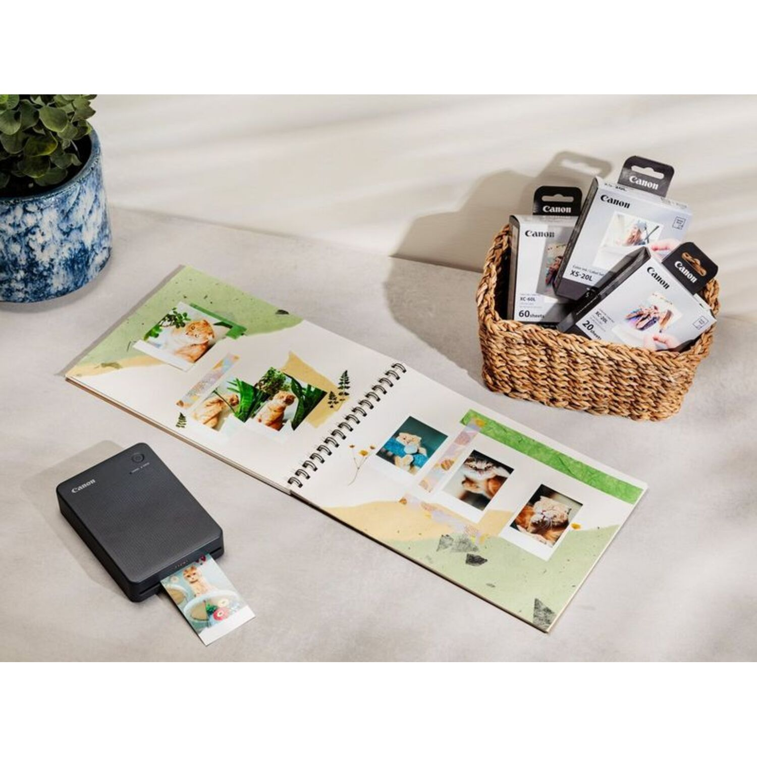 Een draagbare printer drukt een foto af, naast een fotoalbum en inktcartridges.