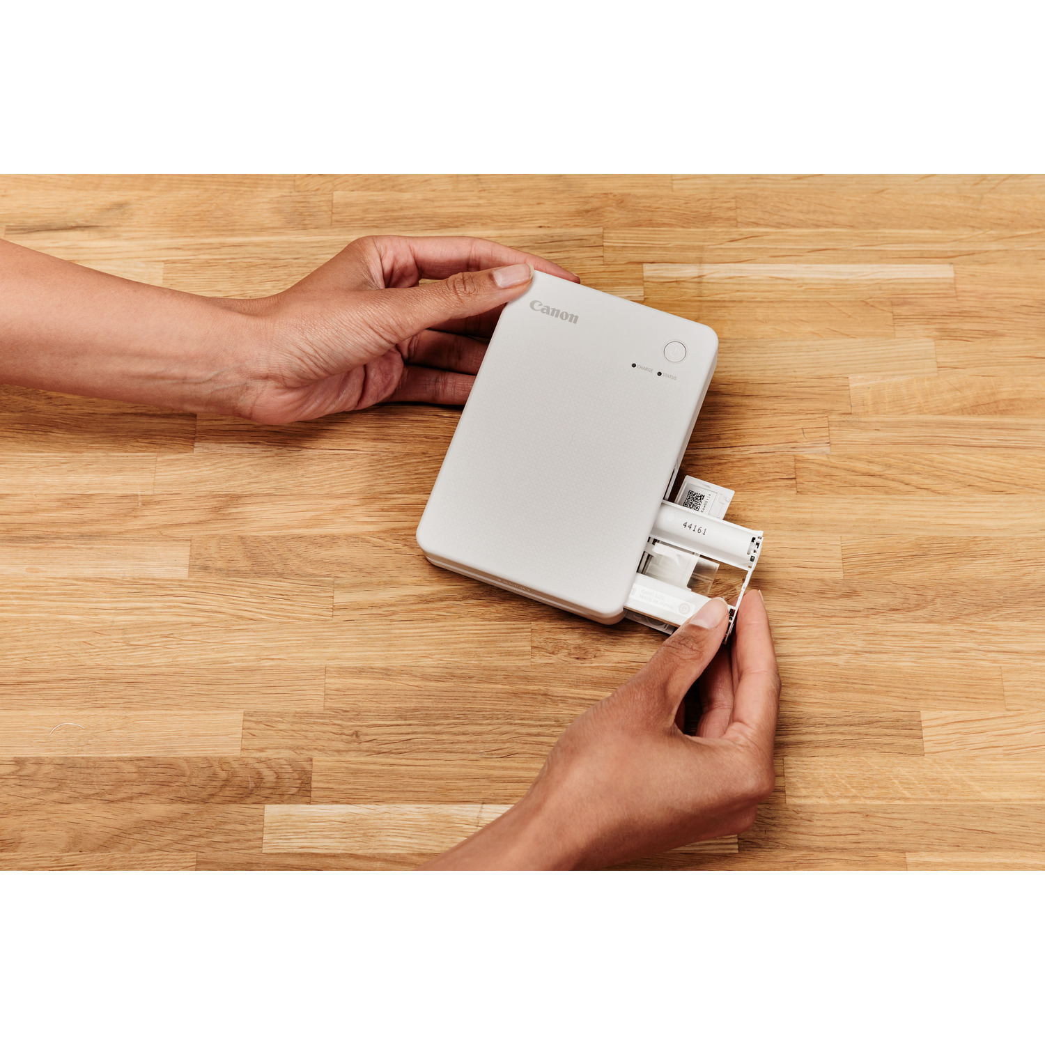 Mains tenant une imprimante Canon blanche, avec une impression photo sortant partiellement.