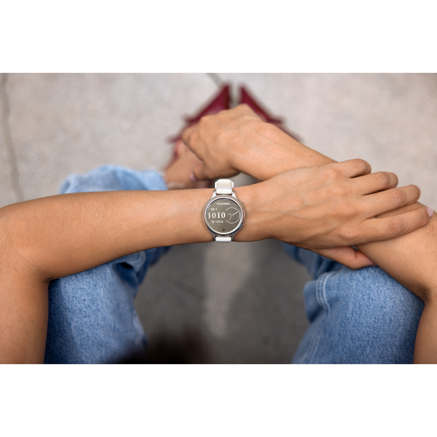 Armen en pols van een vrouw met een Garmin smartwatch. Zittend met gekruiste benen, lichte achtergrond.