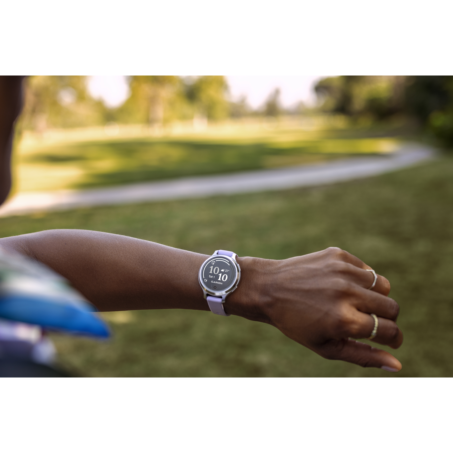 Pols van een persoon met smartwatch, ringen en een vage groene achtergrond.