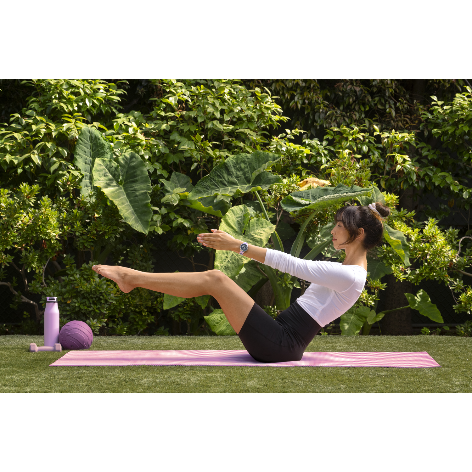 Vrouw doet Pilates op een roze mat buiten. Paarse bal en waterfles in de buurt. Groene achtergrond.
