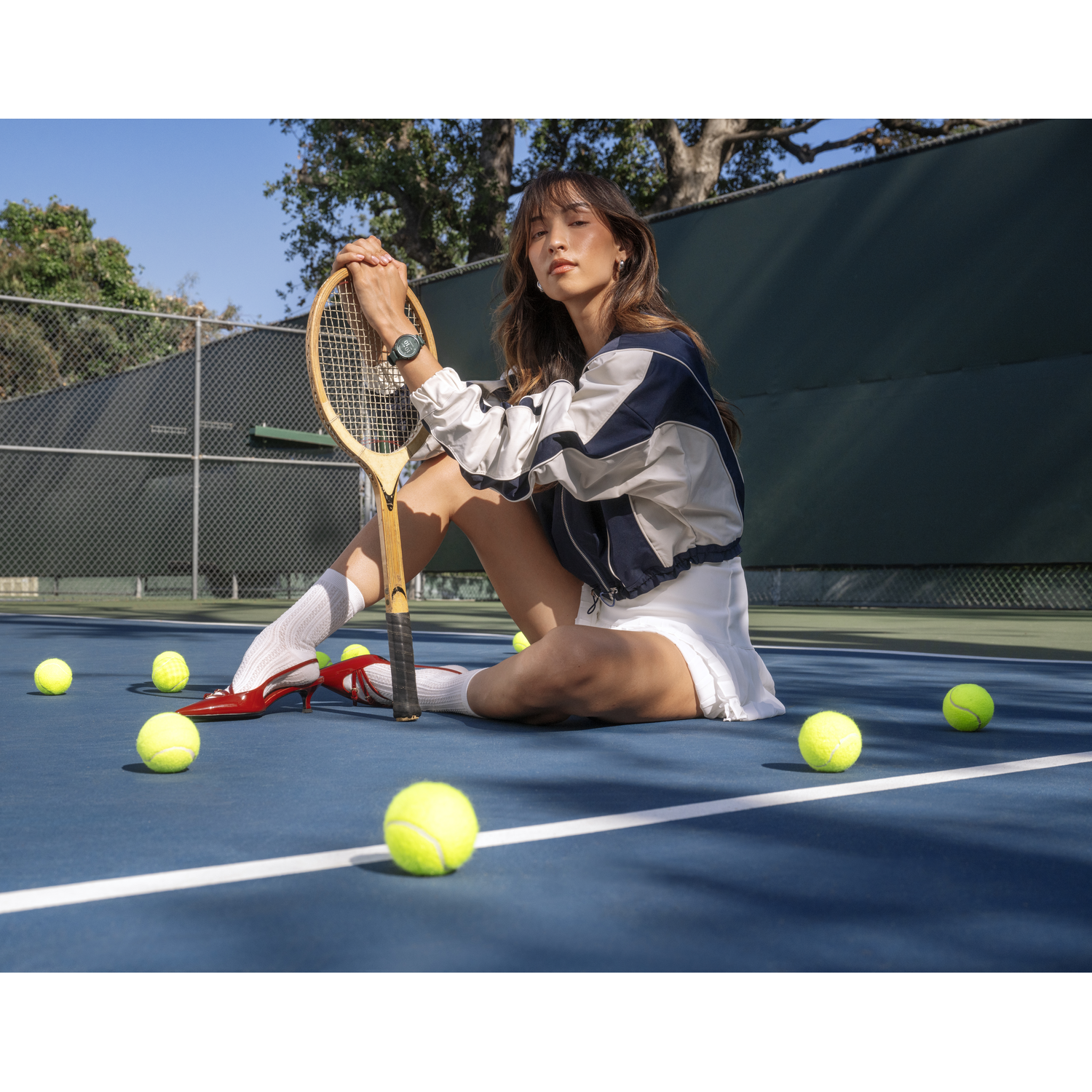 Een vrouw op een tennisbaan met een racket, omringd door tennisballen.