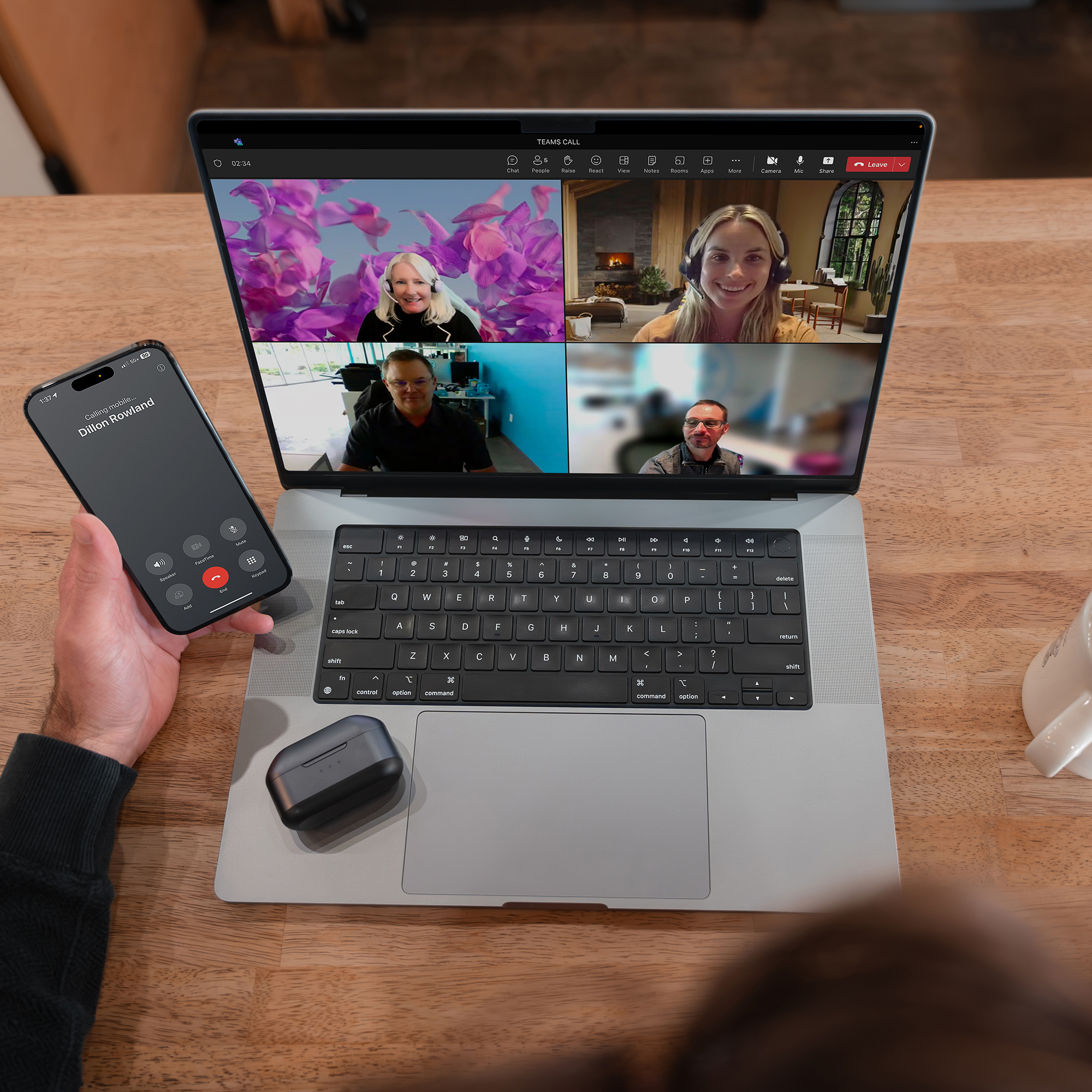 Személy telefonhívással, laptop videóhívással. Fülhallgató az asztalon. Fa asztal háttere.