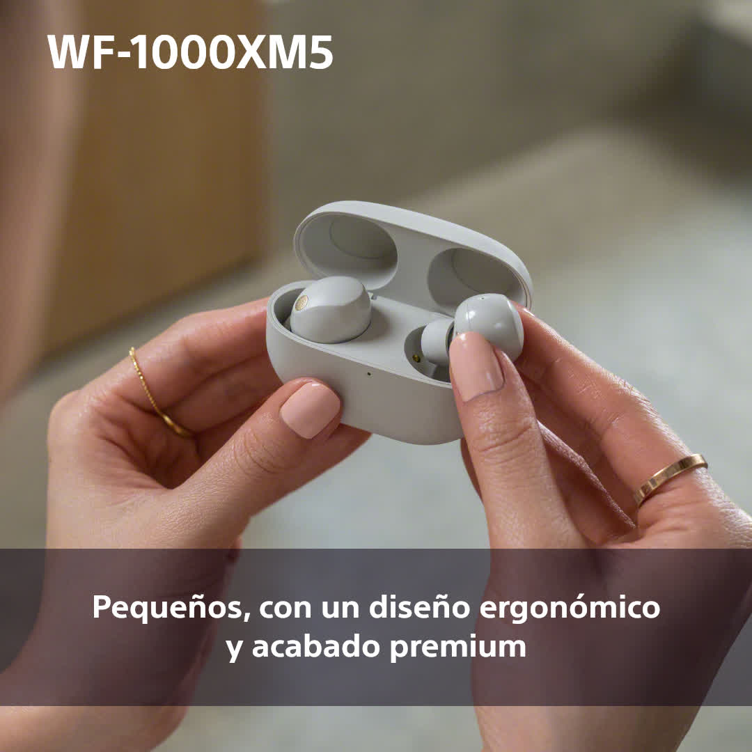 Manos sosteniendo auriculares inalámbricos en un estuche de carga. El estuche está abierto.