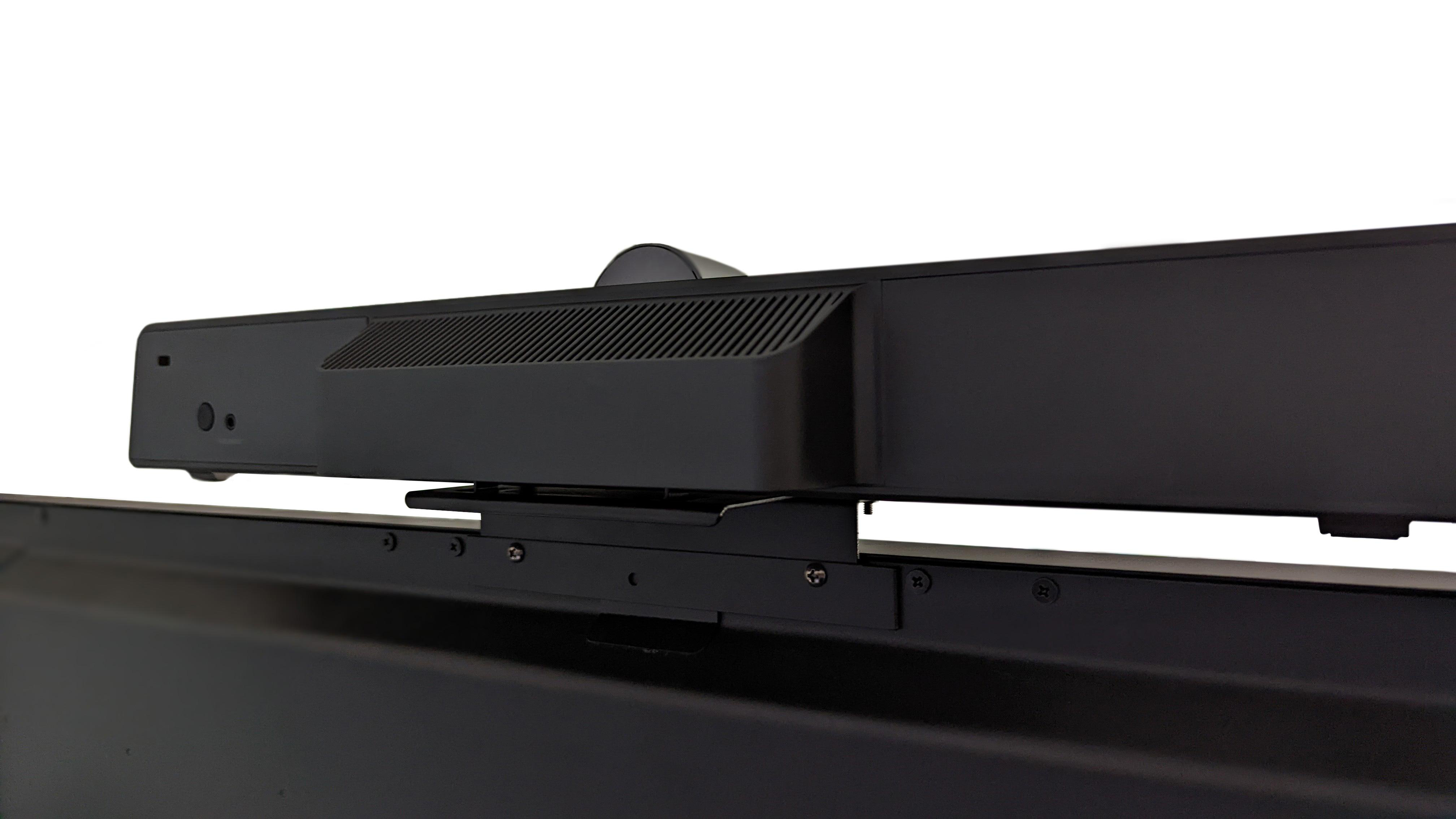 Schwarze Soundbar über einem Bildschirm montiert, mit Kamera und Halterung sichtbar.