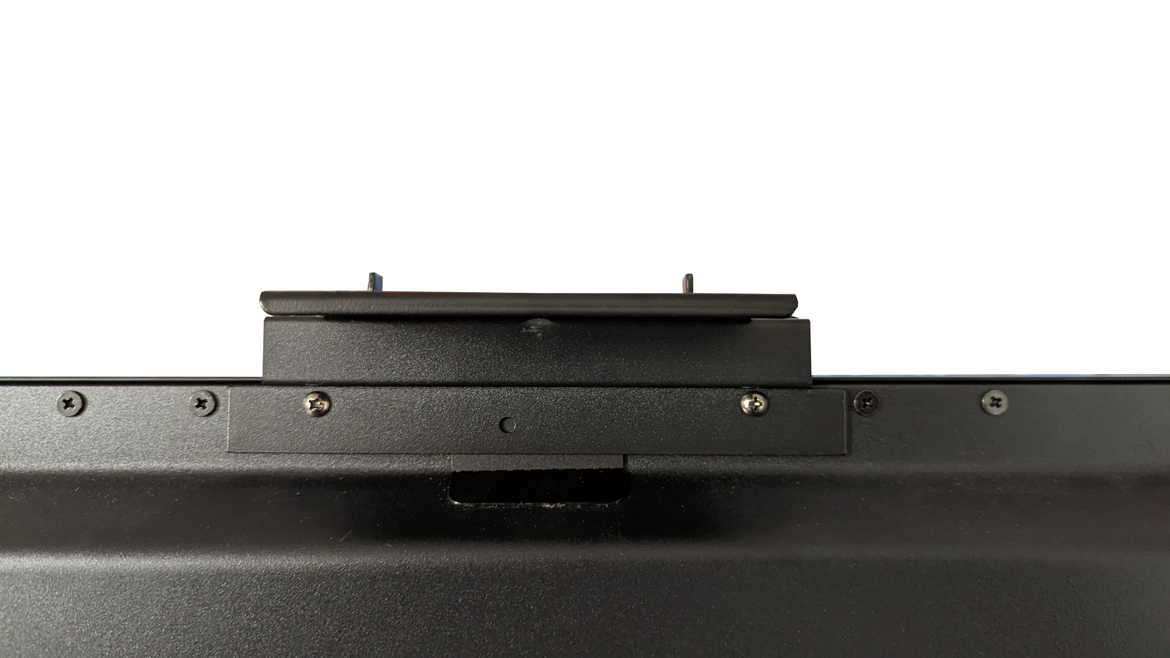 Nahaufnahme einer schwarzen Halterung mit Schrauben, montiert auf einer weißen Oberfläche. Minimalistisch, technisch.