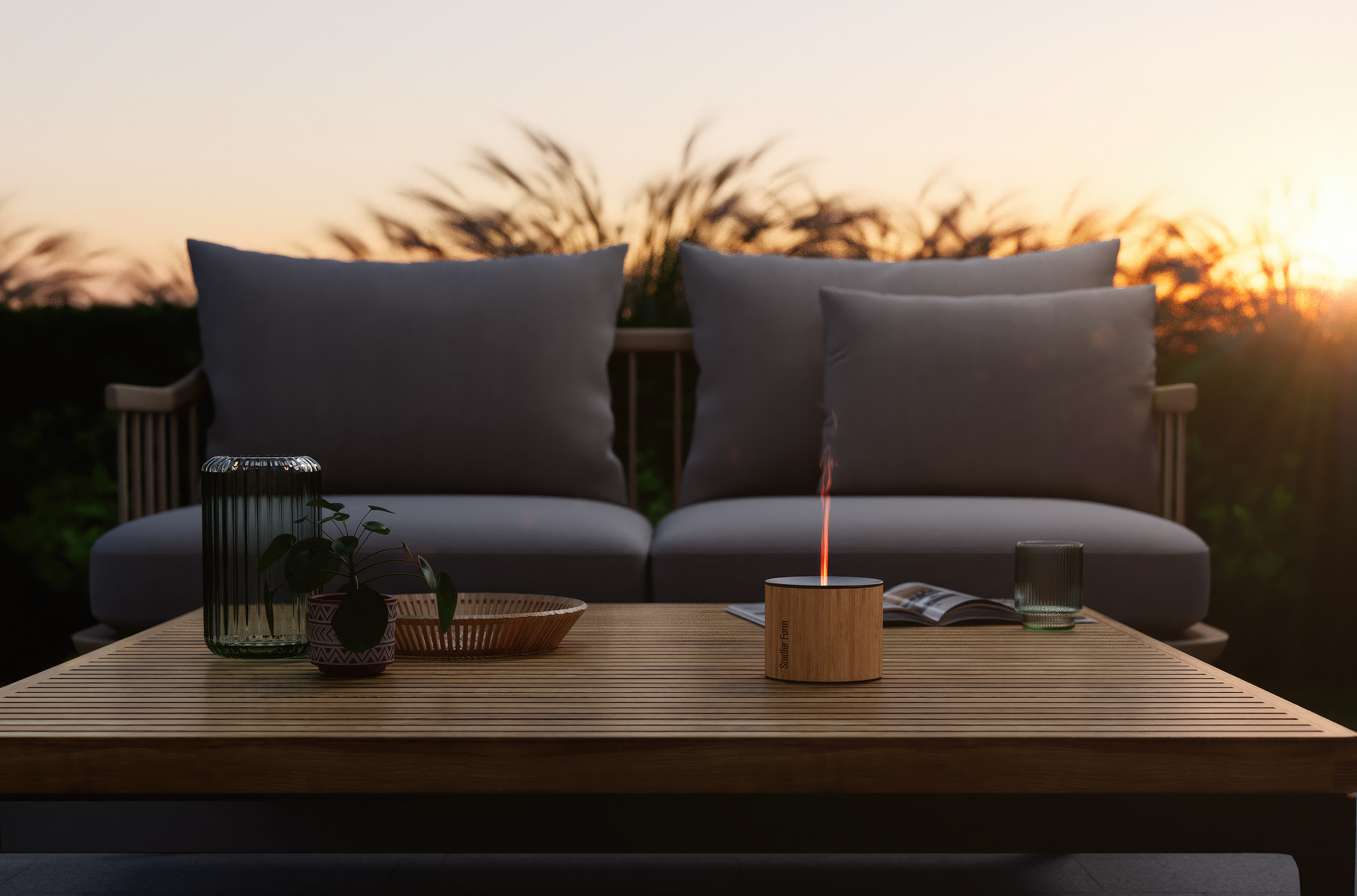 Ein Tisch mit einem beleuchteten Feuerstelle, Gläsern und einem Buch. Sofas sind im Hintergrund bei Sonnenuntergang.