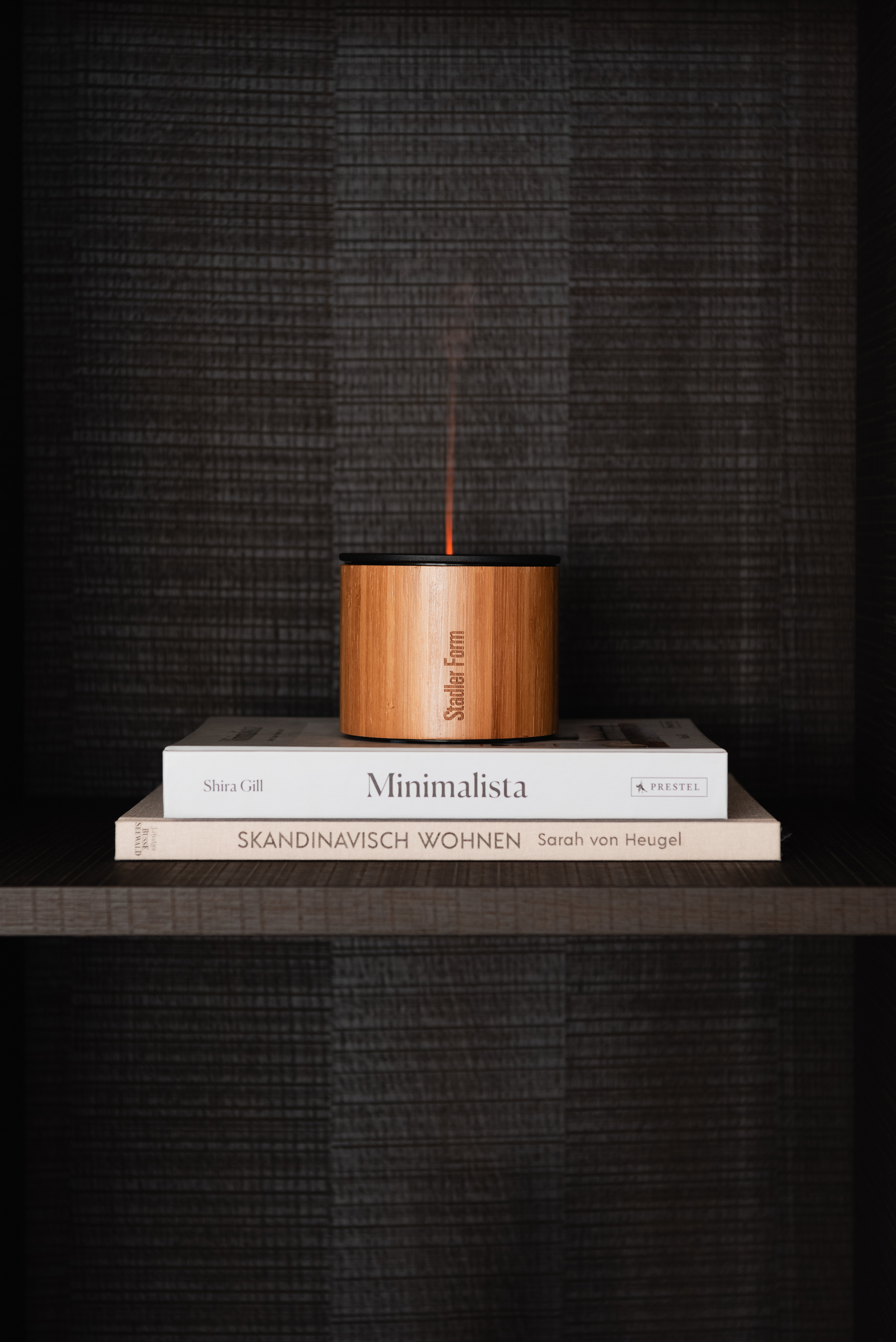 Ein Holz-Studio Farm Diffusor auf Büchern vor dunklem, strukturiertem Hintergrund.