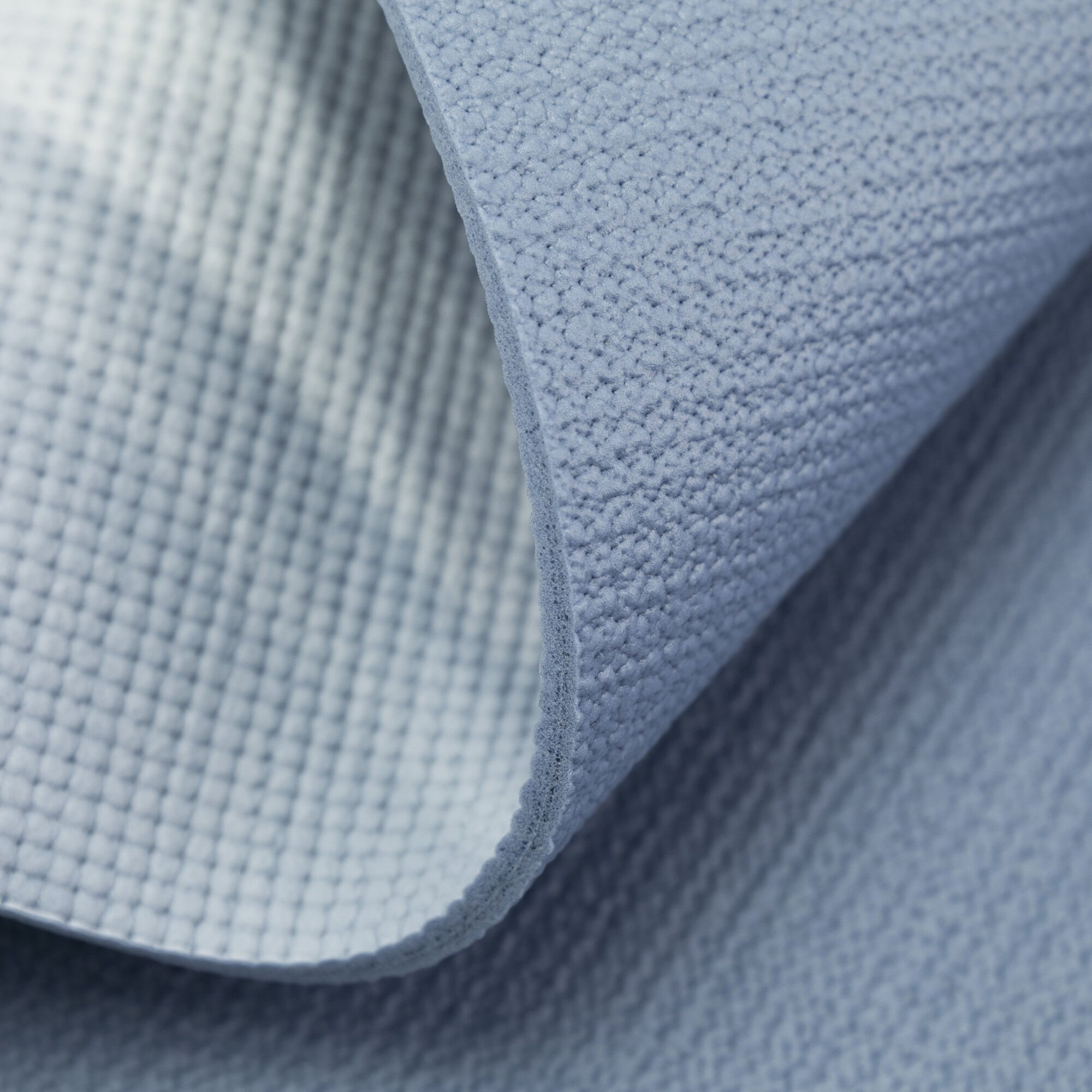 Zbliżenie powierzchni niebieskiej maty do jogi. Mata jest lekko zwinięta.