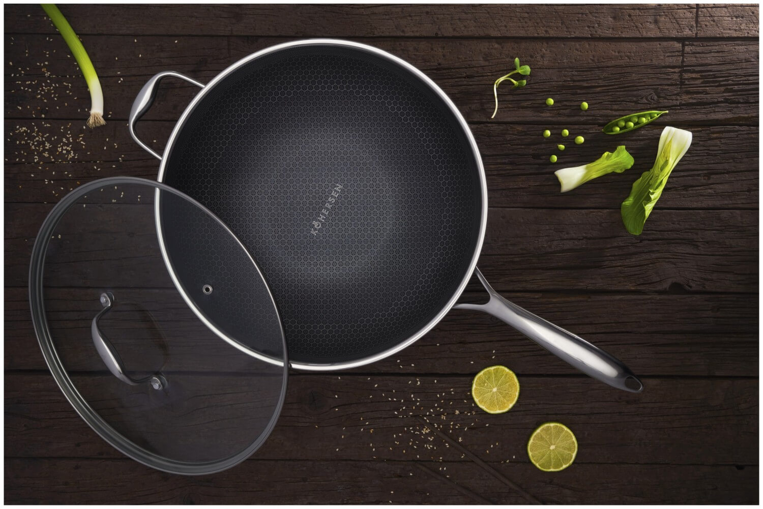 Wok z szklaną pokrywką na drewnianej powierzchni. Warzywa i przyprawy ułożone wokół.